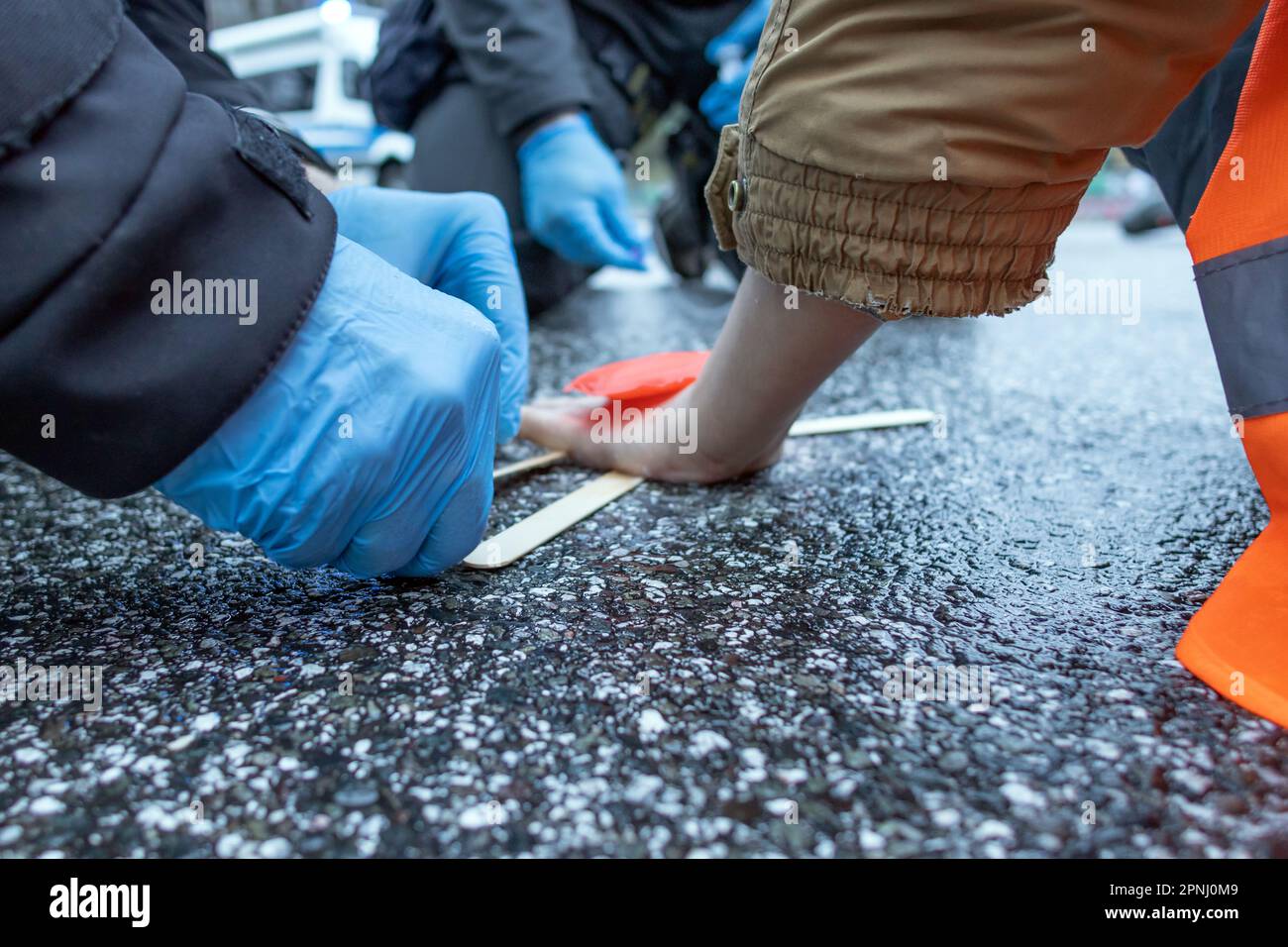 Ein Polizist benutzt Lösungsmittel, um einen verklebten Klimaaktivisten aus dem Asphalt zu entfernen Stockfoto