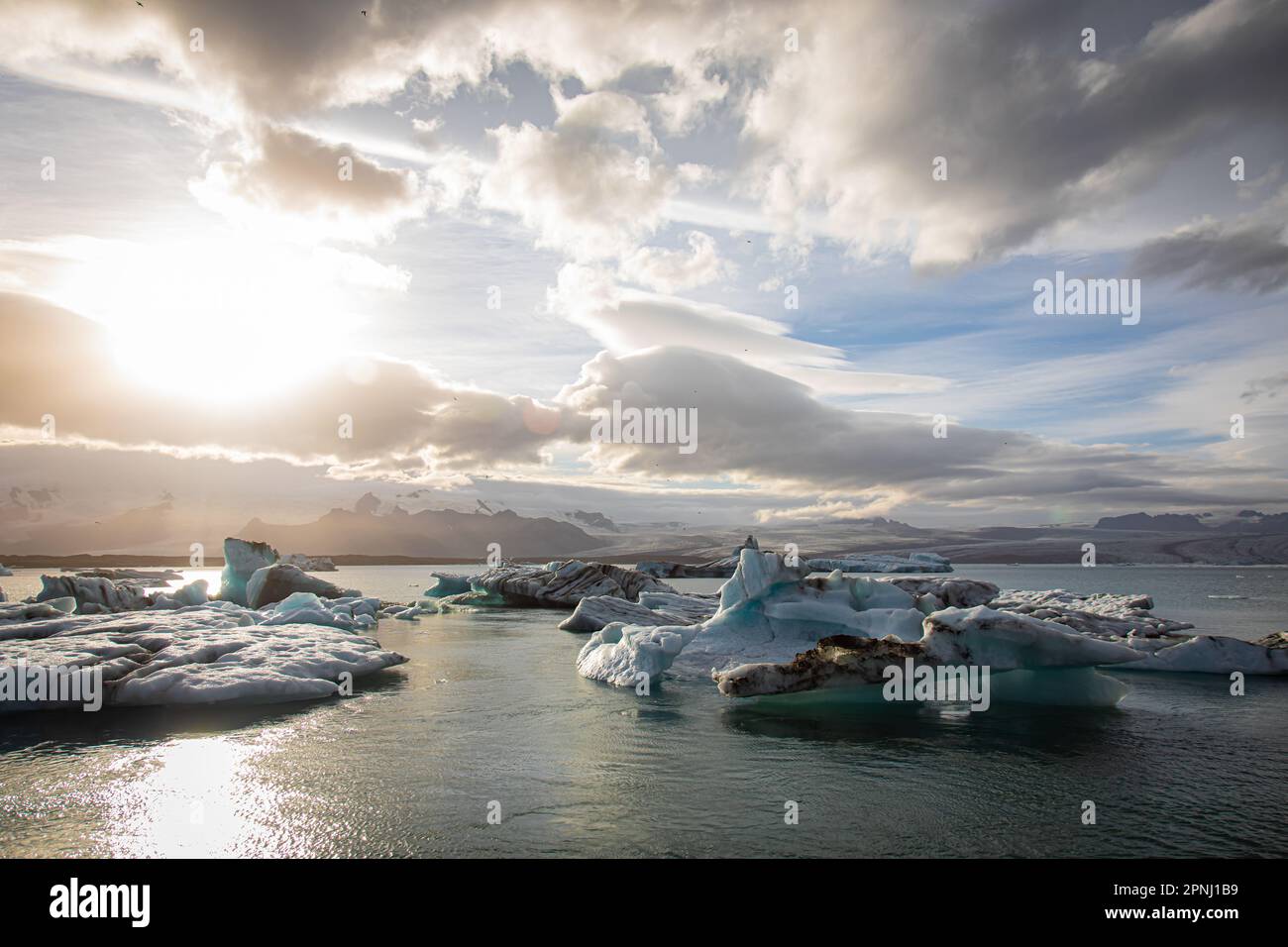 Spektakulärer Sonnenuntergang über der Jokulsarlon Bay in Island, mit Eisbergen, die im gefrorenen Wasser der Eislagune schweben, mit Robben und Vögeln rundherum Stockfoto