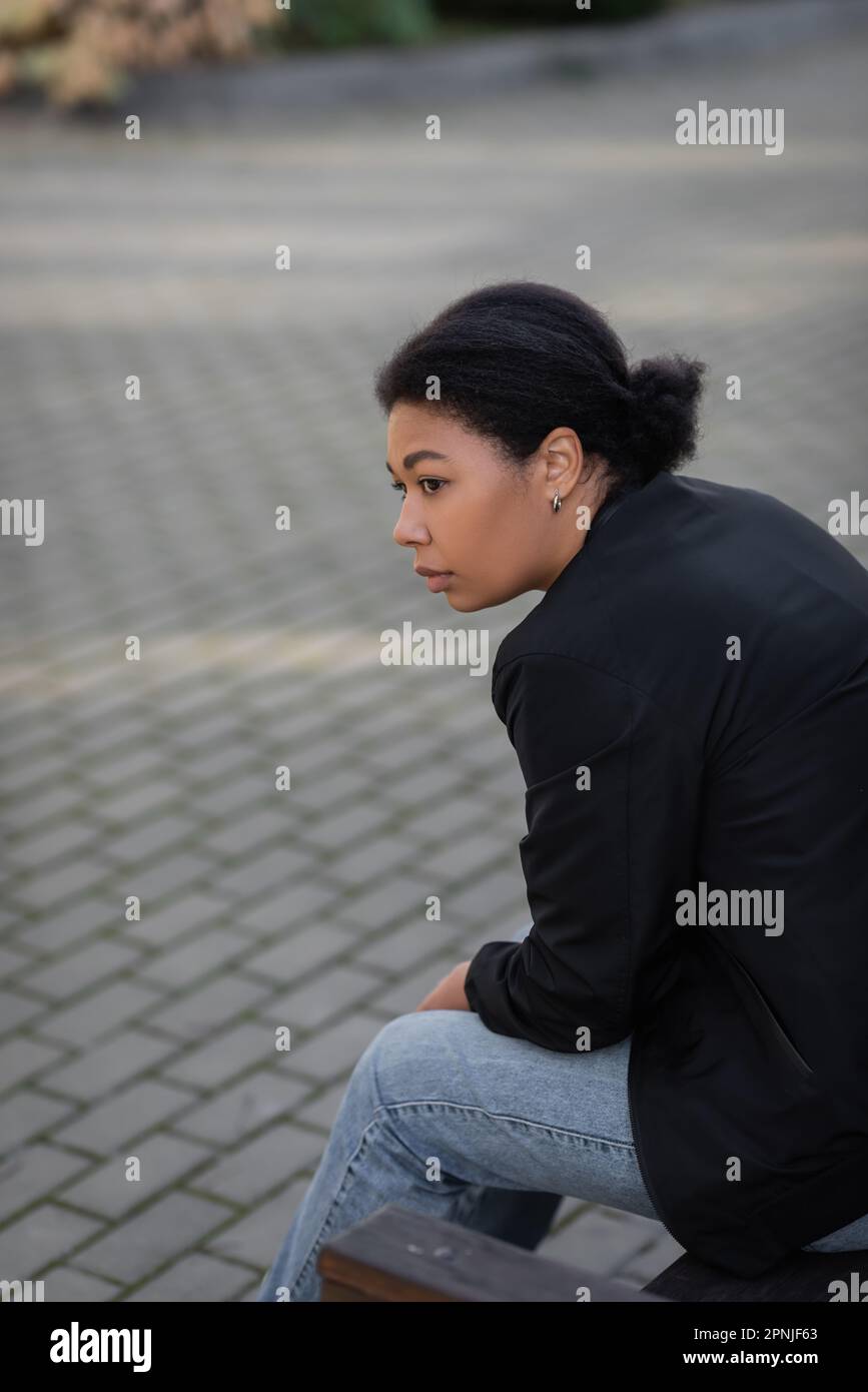 Junge multirassische Frau mit psychischen Problemen, die draußen auf einer Bank sitzt, Stock Image Stockfoto