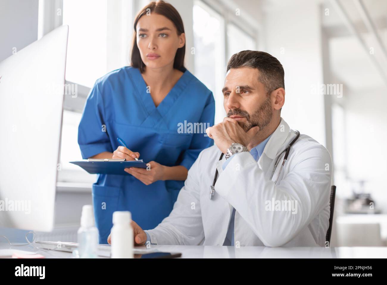 Fokussierte zwei Ärzte, die sich Computerbildschirme ansehen, die Krankheiten oder Diagnosen des Patienten diskutieren, in der Klinik zusammenarbeiten Stockfoto