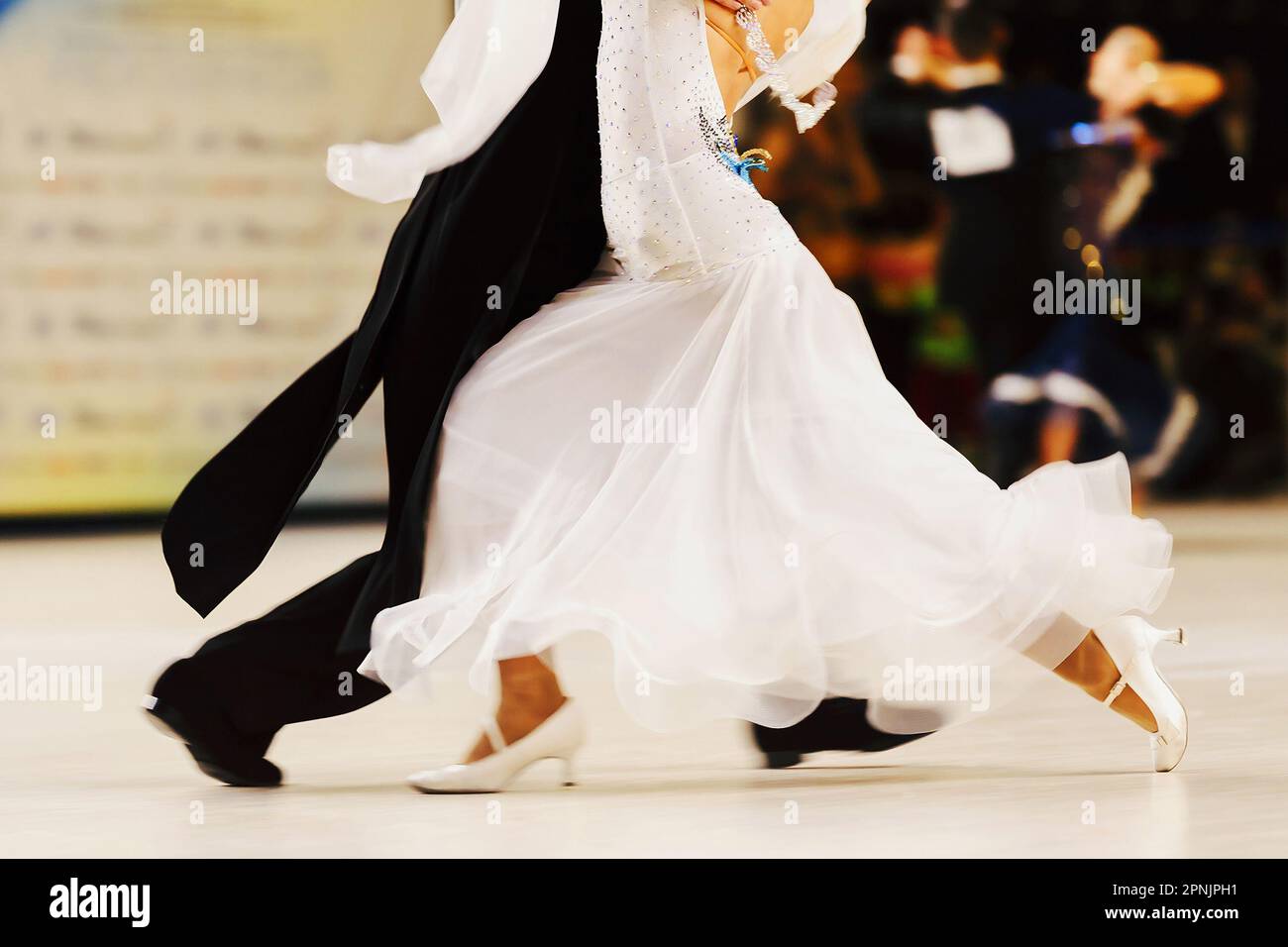 Partner tanzt Tango im Tanzsaal, Frau trägt weißes Kleid und schwarzen Schwanzanzug auf Mann Stockfoto