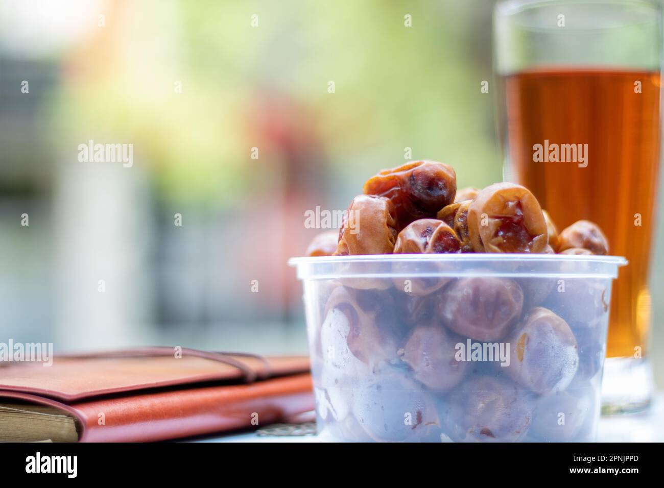 Braune Palmendaten und ein Notizbuch und ein Glas Eistee mit Hintergrundunschärfe. Eine süße Dattelpalme Stockfoto