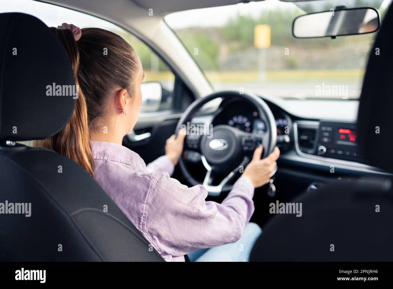 Frau, die Auto fährt. Junger Fahrer. Fahrzeugtest im Händlerbetrieb oder Schülerschulung in der Schule, um eine Lizenz zu erhalten. Hände am Lenkrad. Stockfoto