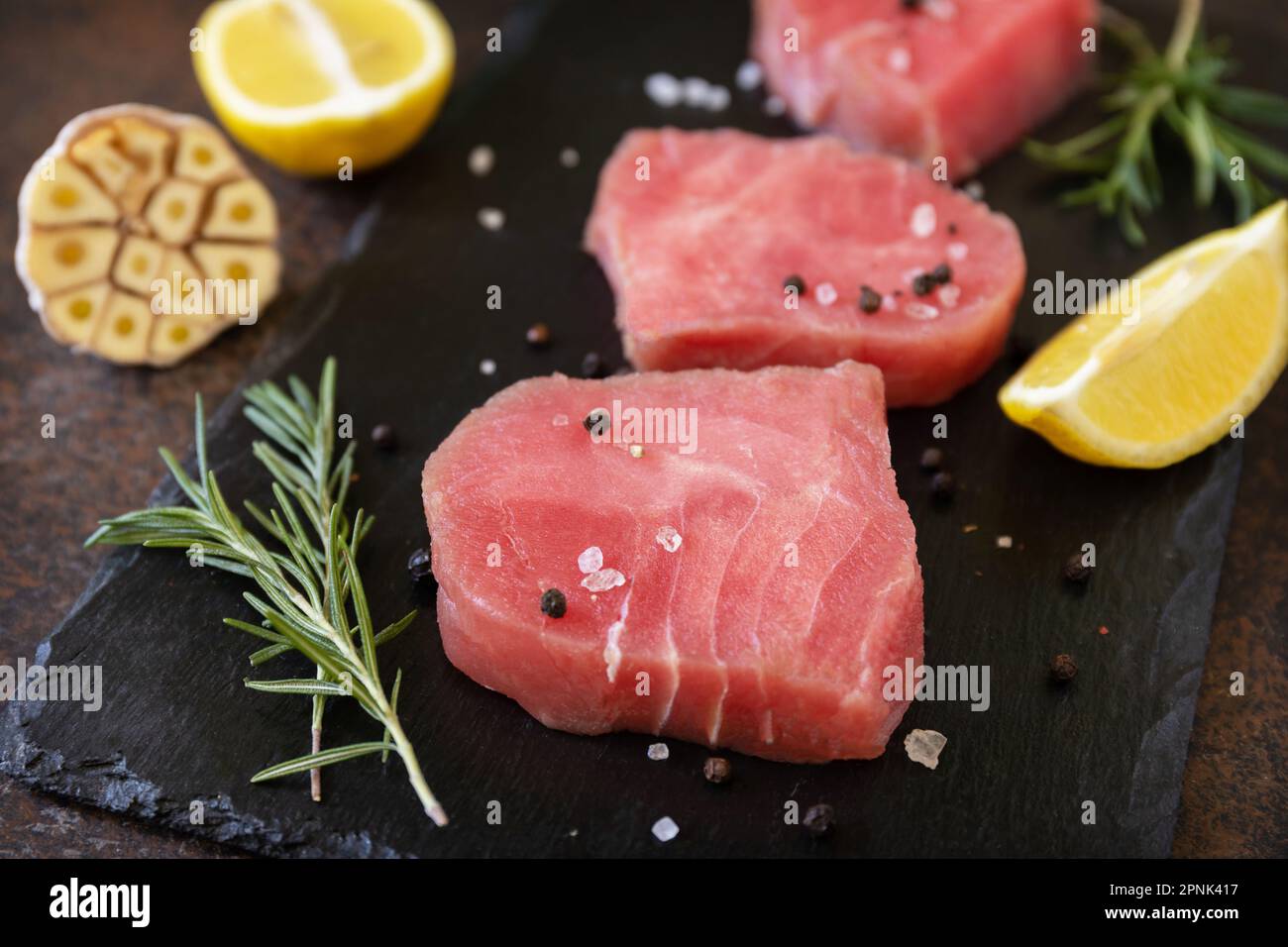 Meeresfrüchte. Rohe saftige Thunfischsteaks mit Gewürzen und Rosmarin auf einem Steintisch. Stockfoto