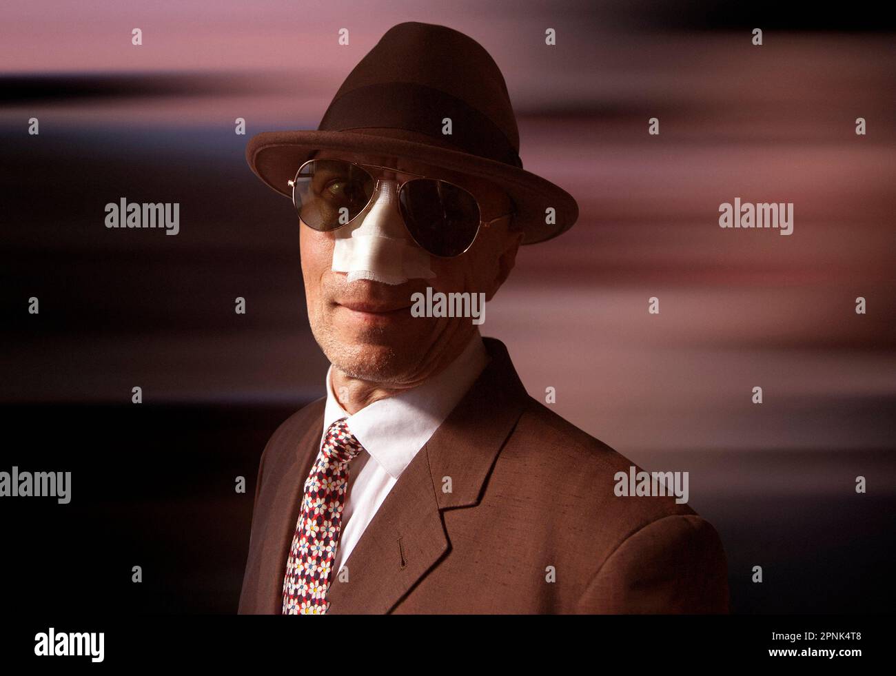 Mann in Anzug, Hut und Sonnenbrille mit Verband an der Nase Stockfoto