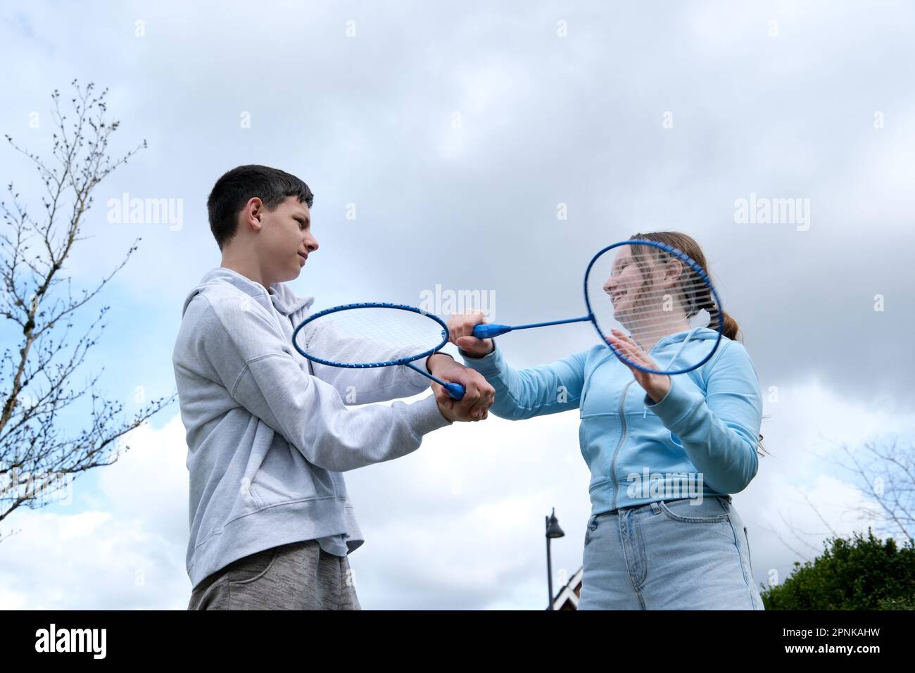 Badminton Schläger Jungen Mädchen schwingen sich mit Schläger Hintergrund des Himmelsspiels Spaß erste Liebe Teenager Beziehung wütend zufrieden Lächeln Emotionen Übergangsalter junge Männer und Frauen Stockfoto