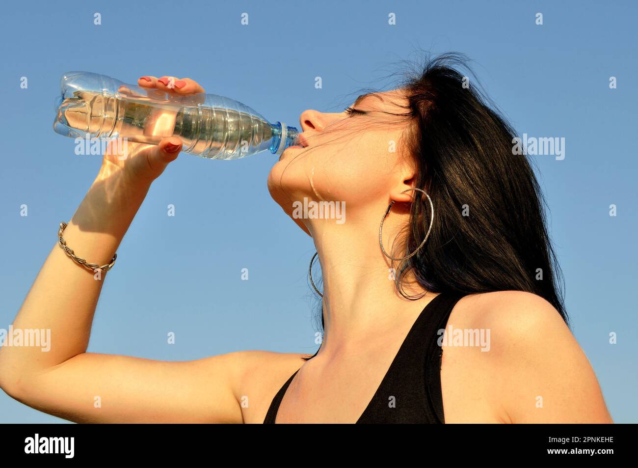 Junge attraktive Frau trinkt kaltes Wasser an heißen Tagen auf blauem Himmel Hintergrund Stockfoto