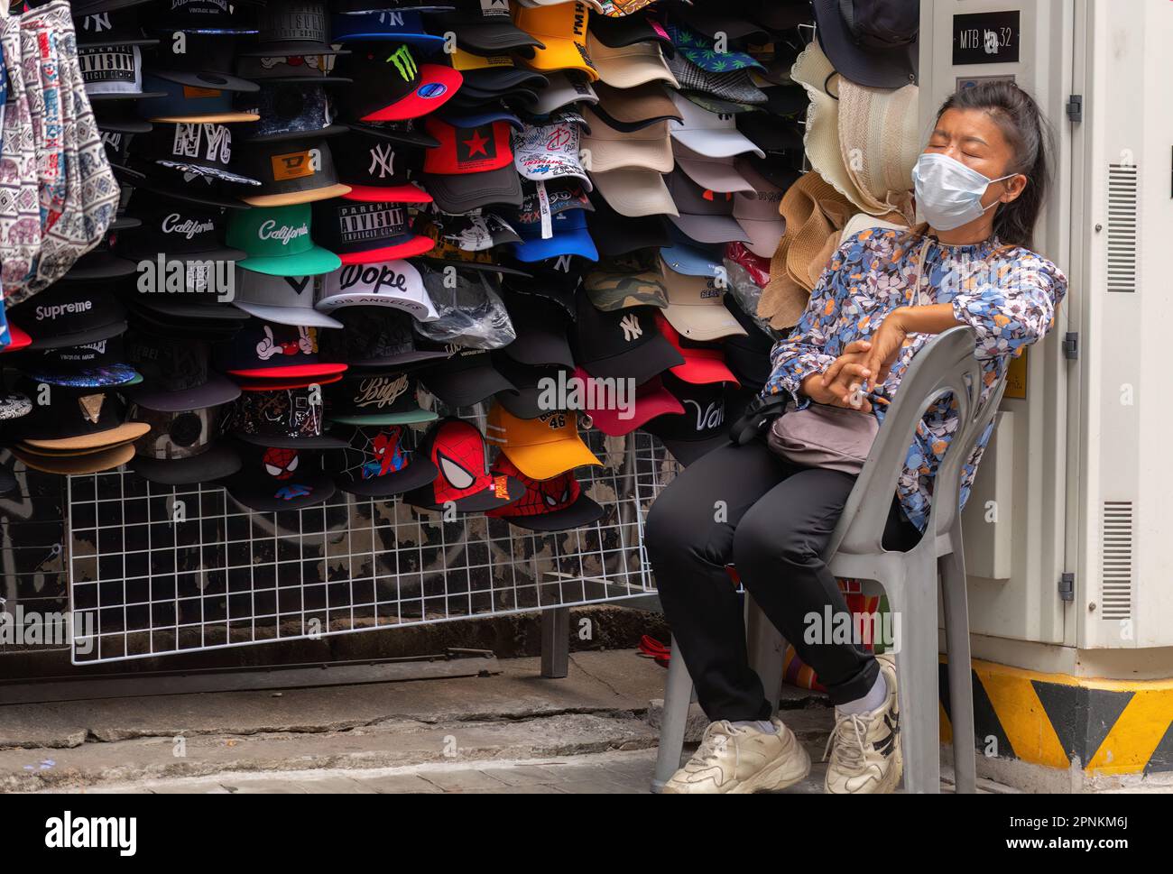 Pattaya, Thailand - März 14,2023: Walking Street eine ältere Thai-Frau schlief auf einem weißen Stuhl, bevor sie anfing, farbenfrohe Hüte für Tour zu verkaufen Stockfoto