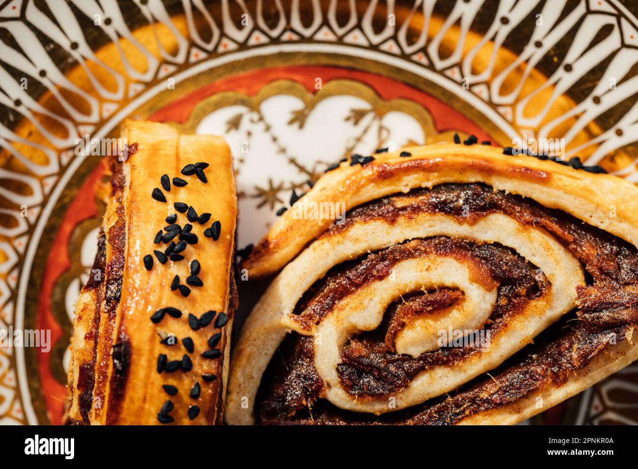 Kleicha, irakische Datteln Kekse in spiralförmiger Form mit Nigellasamen auf einer kunstvoll verzierten goldenen Platte Stockfoto