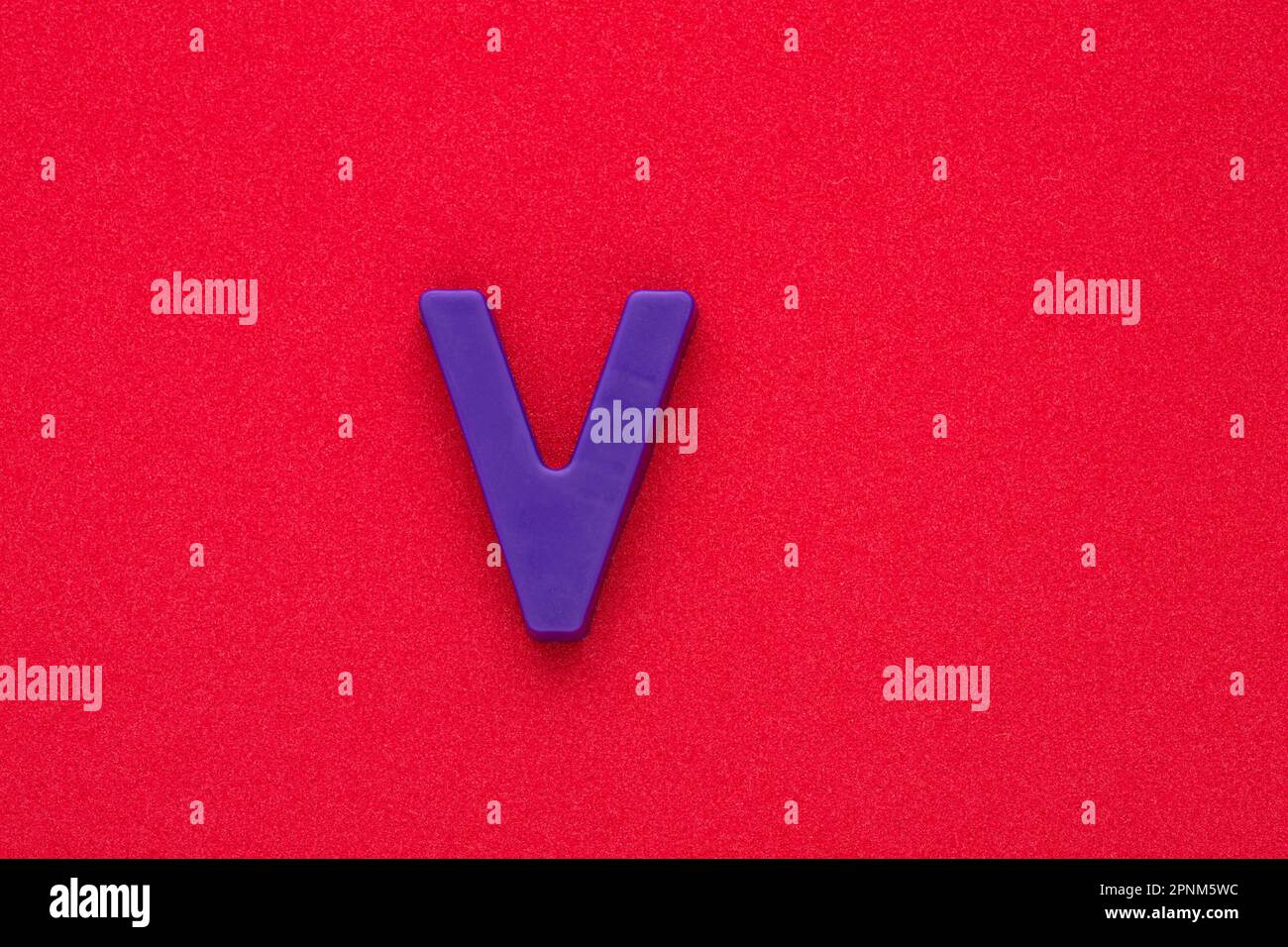 Buchstabe V – Violetfarbenes Kunststoffteil auf rotem, schaumigem 032-C-Hintergrund Stockfoto