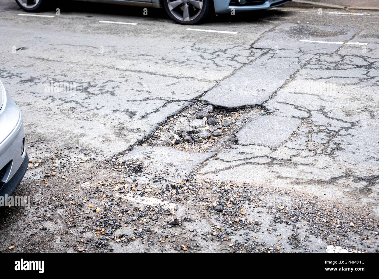 Blick auf ein großes Schlagloch in einer Wohnstraße, Asphalt gebrochen mit einem großen Loch in der Oberfläche Stockfoto