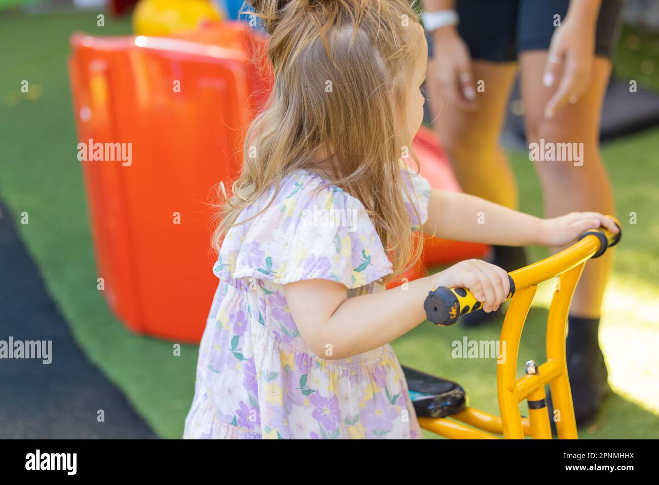 Kinder im Vorschulalter fahren mit dem Fahrrad in einem lebhaften Kindergarten im Freien Stockfoto