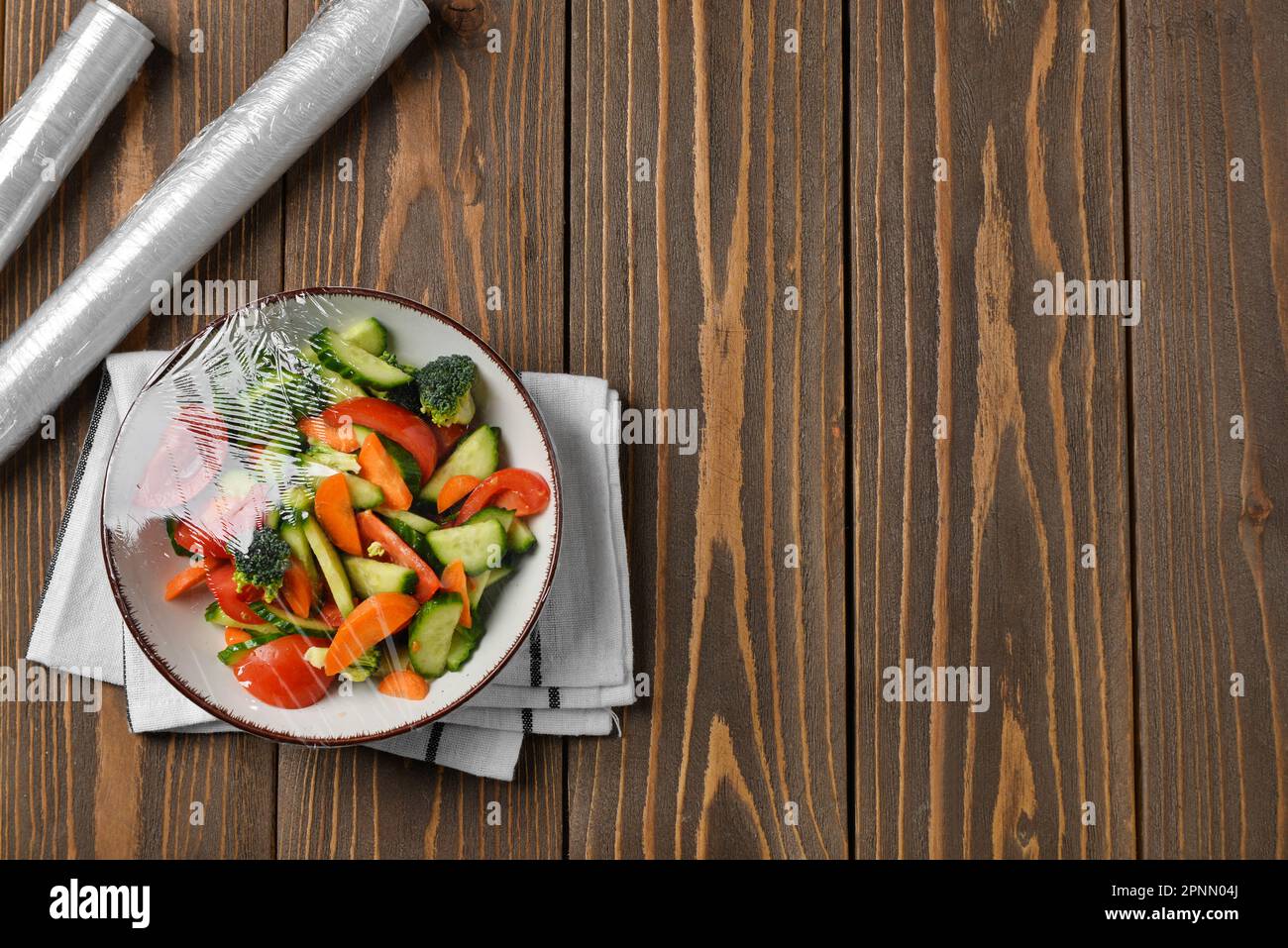 Schüssel mit Salat, mit Stretchfolie auf Holzhintergrund verpackt Stockfoto