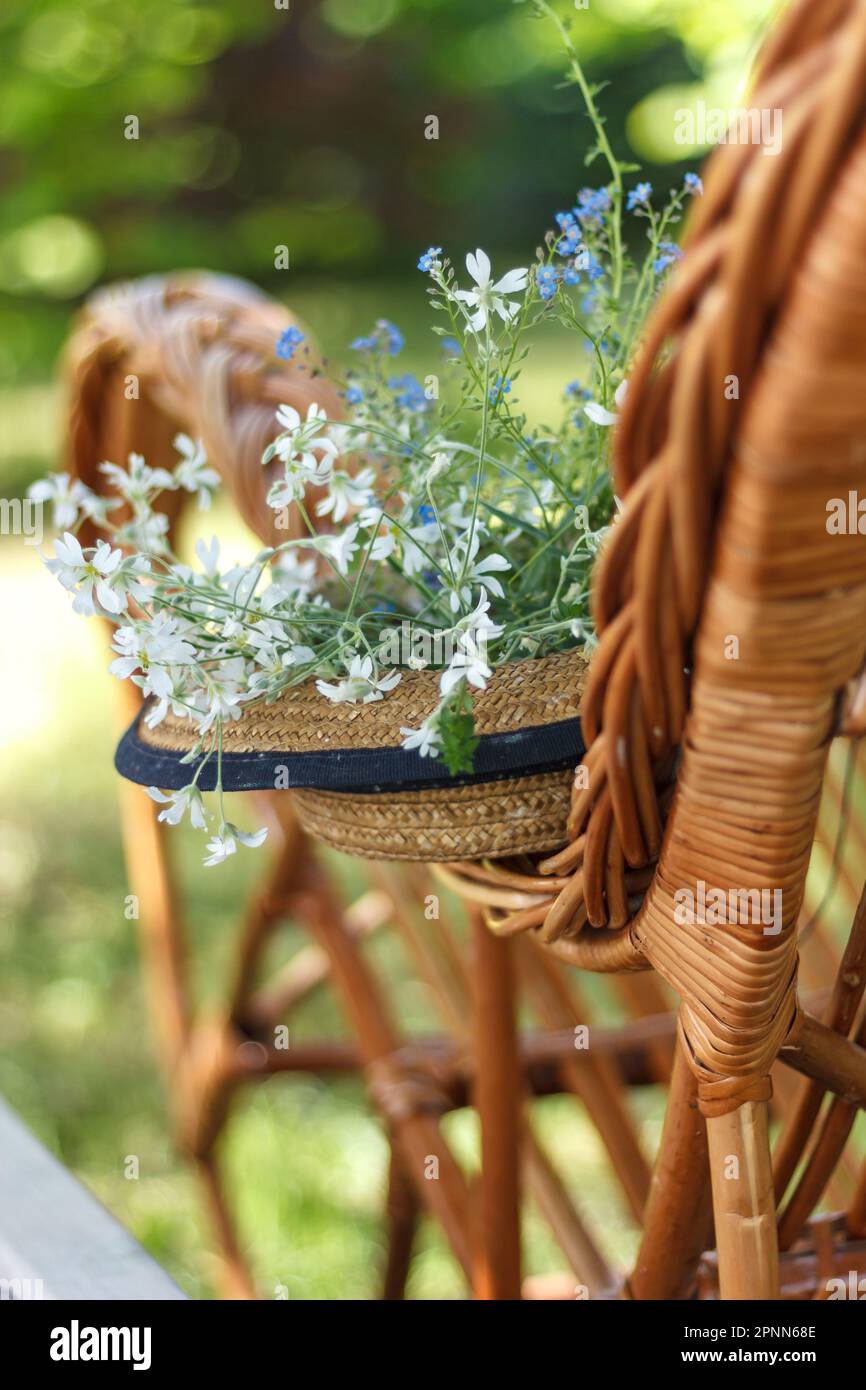 Langsames Leben. Strohhut auf einem Korbstuhl im Garten. Romantische Sommerszene Stockfoto