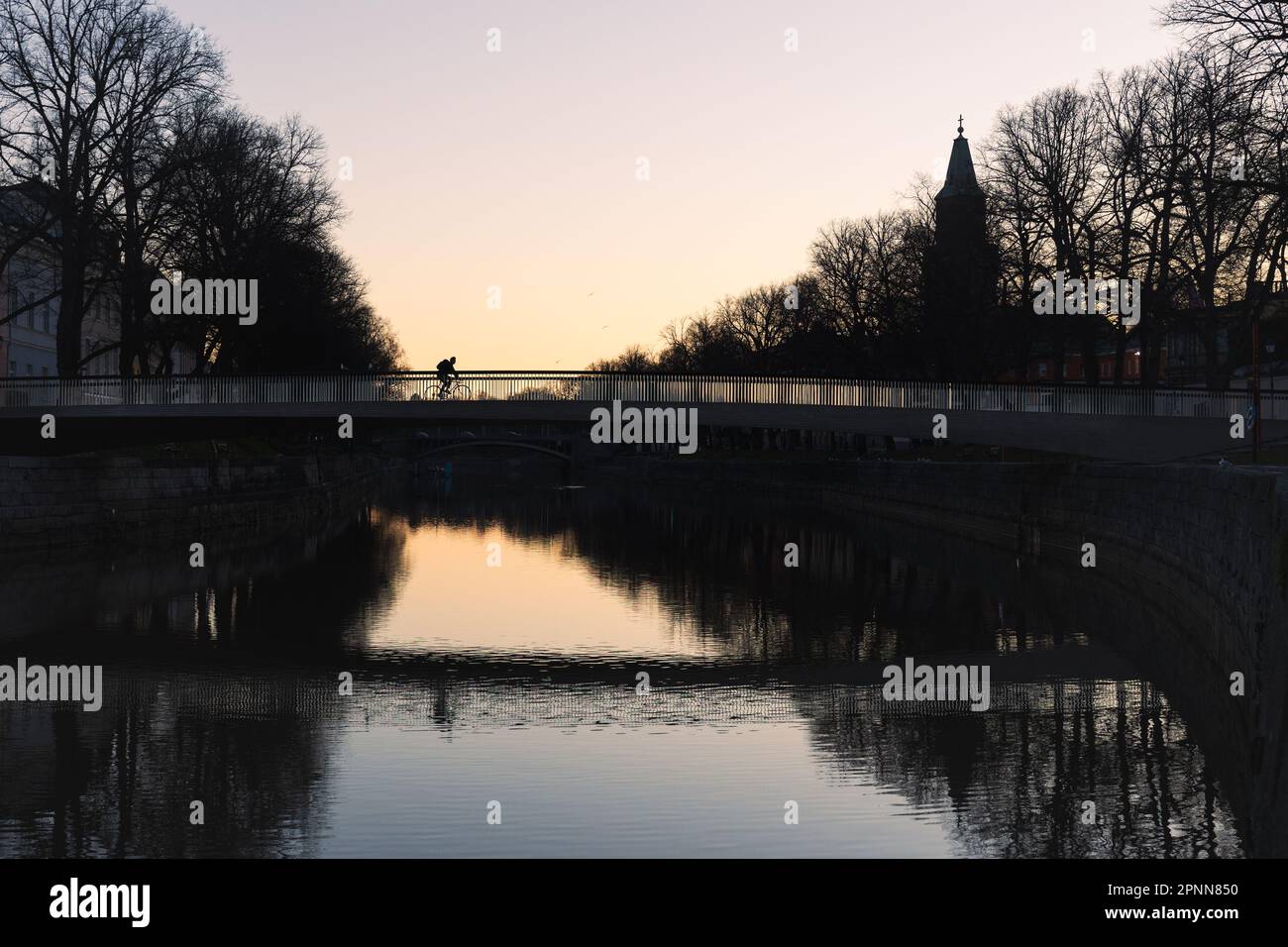 Silhouette einer Person mit Fahrrad auf der Kirjastosilta-Brücke mit dem Turm der Turku-Kathedrale im Hintergrund in Turku, Finlandin Frühlingsmorgen Stockfoto