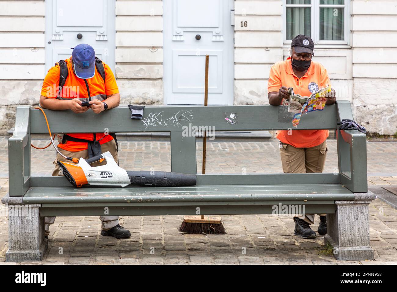 Zwei Mitarbeiter des Reinigungsdienstes der Stadt Brüssel lehnen sich auf eine öffentliche Bank und machen Pause. Stockfoto