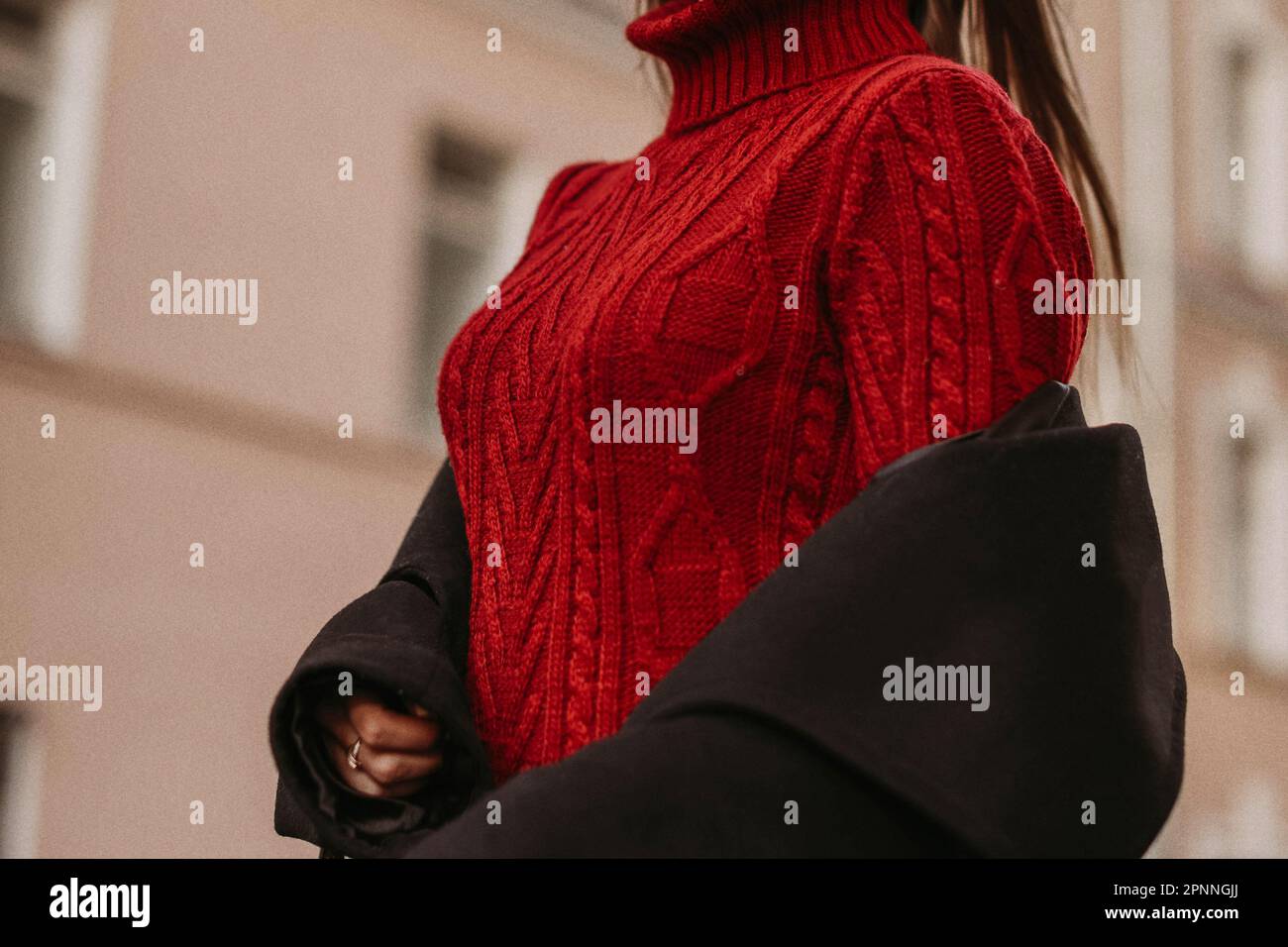 Weibliche Figur im roten, warmen Strickpullover und schwarzen Mantel. Porträt im Freien bei Tageslicht. Stoffkonzept im Herbst-Winter-Straßenstil Stockfoto