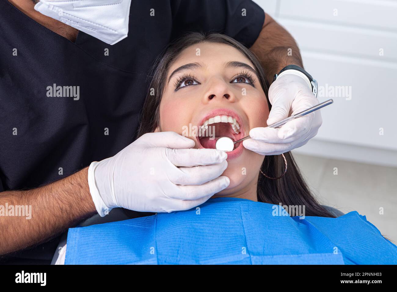 Der hohe Winkel des Teenager-Patienten, der den Mund öffnet, während der Zahnarzt bei der Zahnarztuntersuchung während der Zahnkliniktermine den Spiegel benutzt Stockfoto