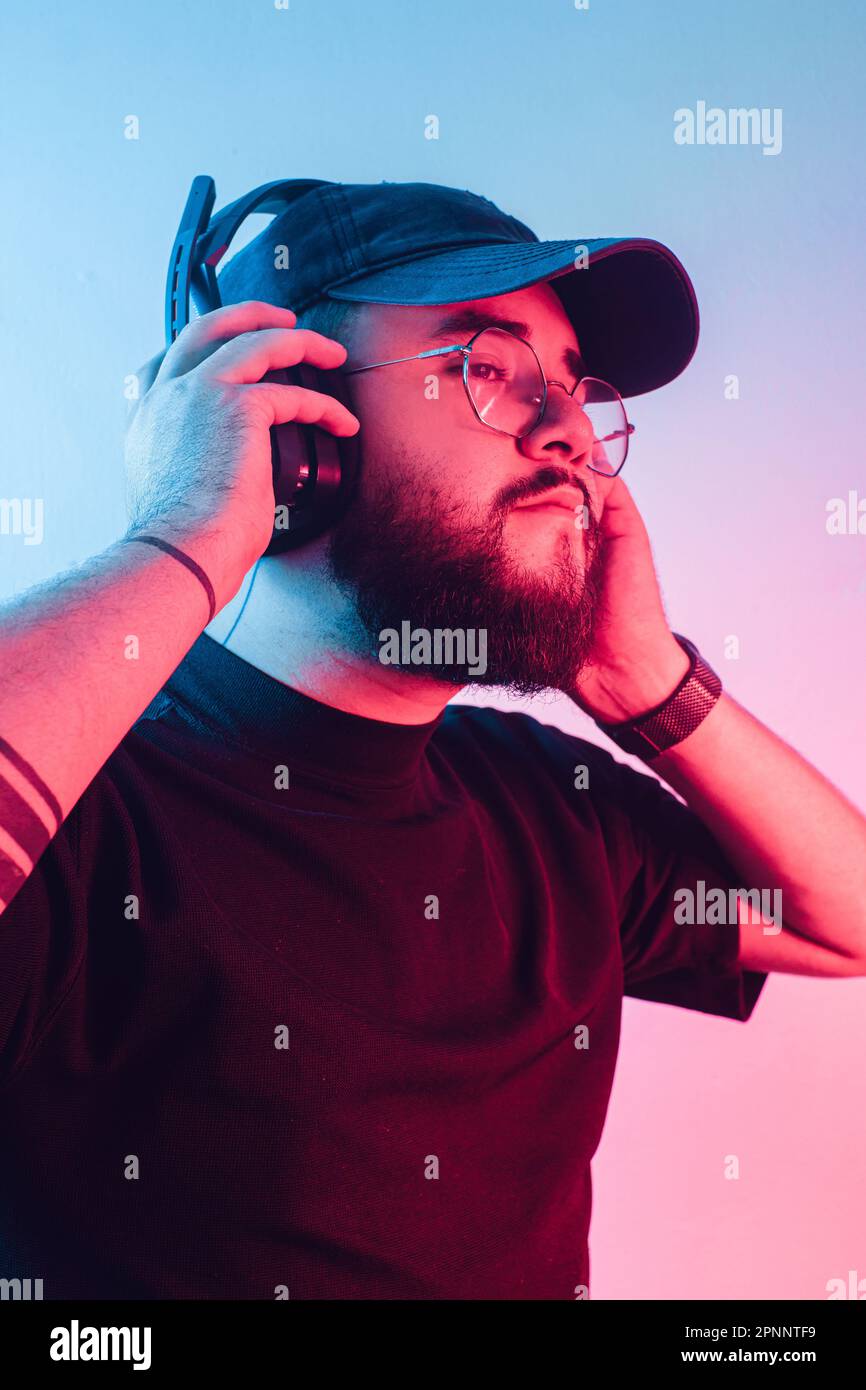 Junger lateinamerikanischer Mann mit Bart und Brille, der einen Kopfhörer zum Spielen hält. Stockfoto