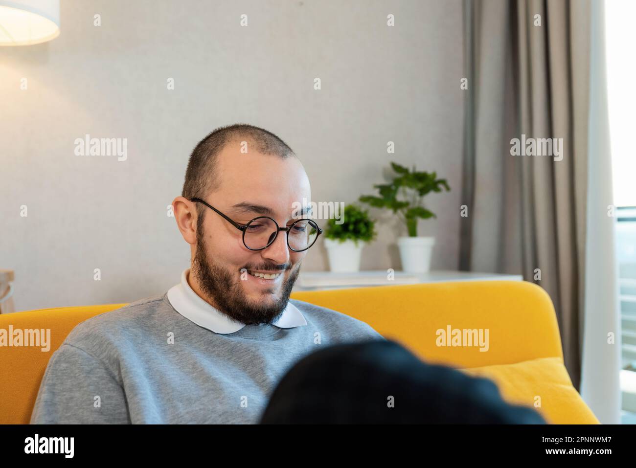 Junger attraktiver Hipster mit Brille, der zu Hause auf dem Sofa auf dem Handy sitzt. Schüler, die Smartphone-Gadget verwenden, mobile Social-Media-App Stockfoto