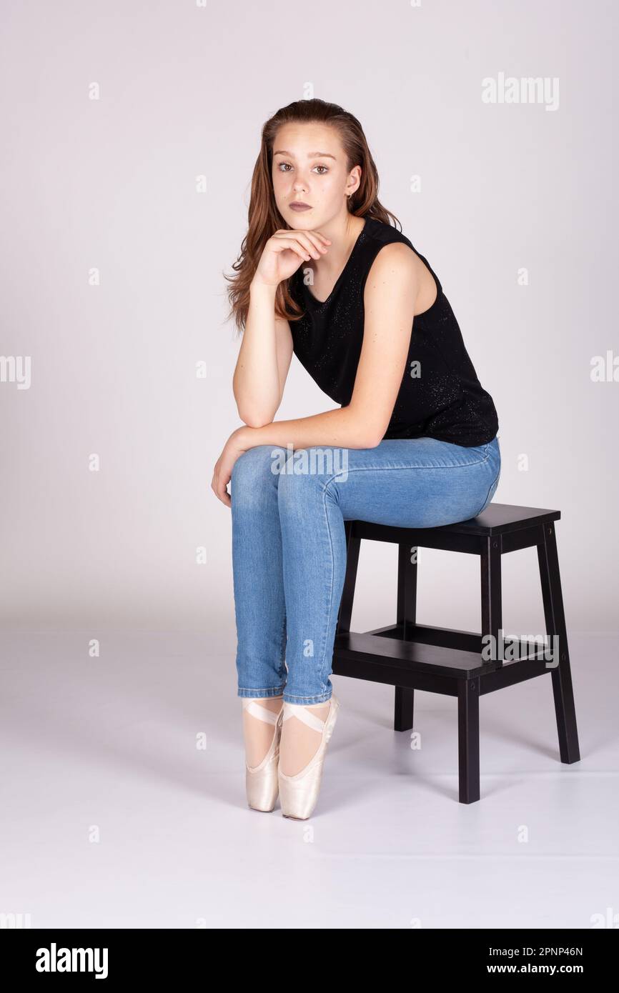 En Pointe ruht sich auf Hocker Beine zusammen en pointe wunderschönes Teenager Mädchen sitzt gerade und schaut in die Kamera, Hand an Kinn mit einem intimen Blick. Stockfoto