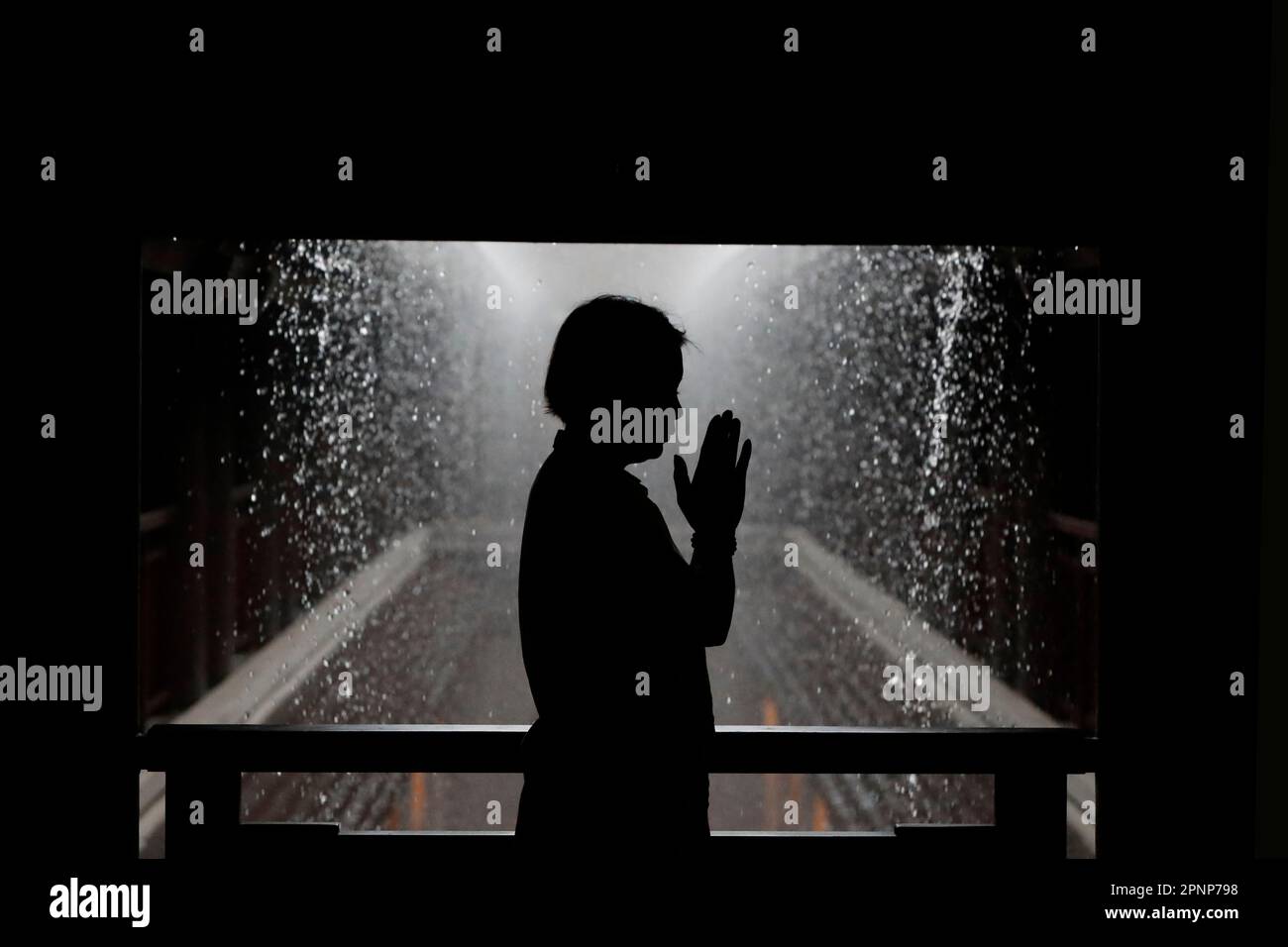 Schwarz-weiße Silhouette einer Frau, die während der Regenzeit betet. Stockfoto