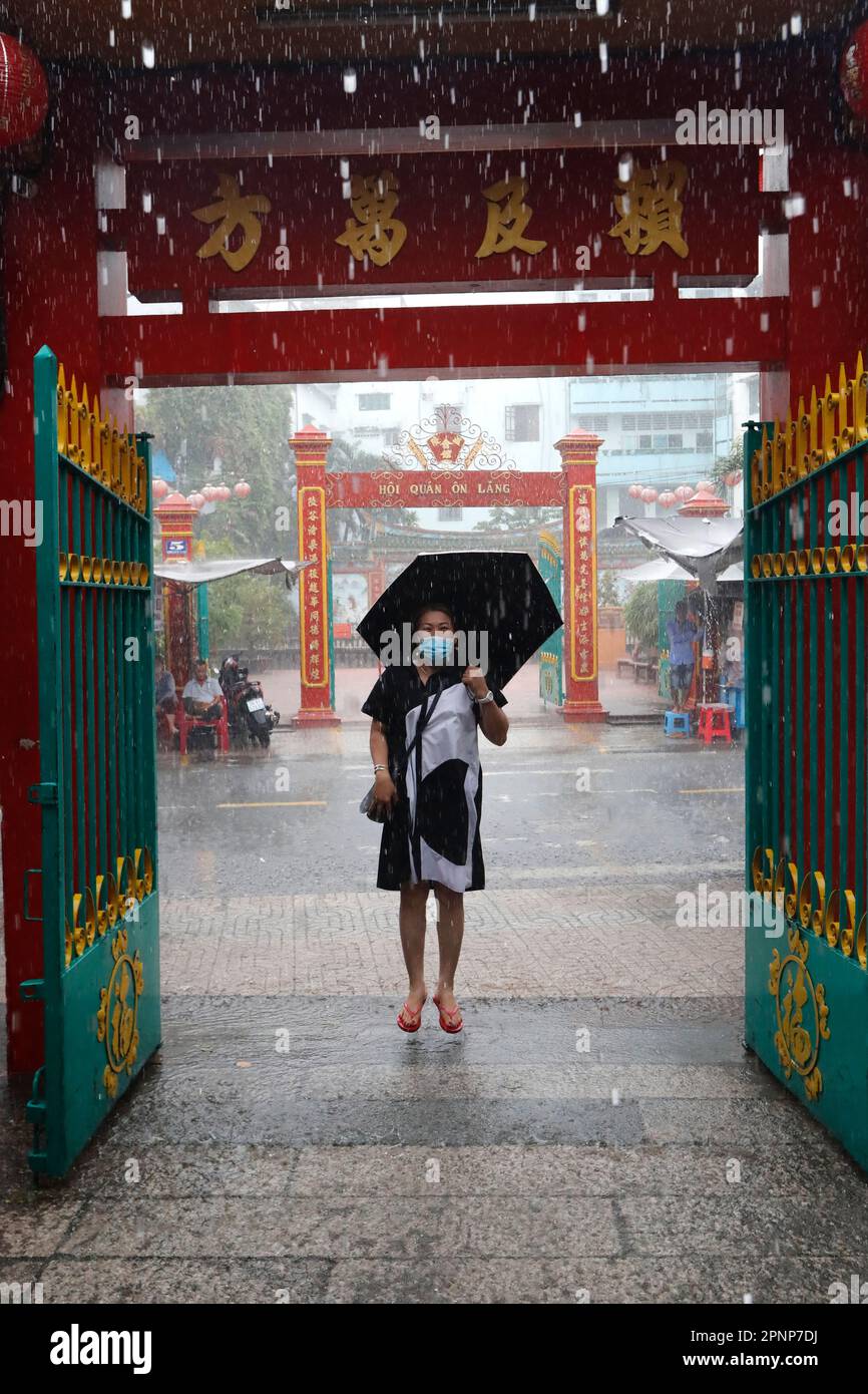 Quan am buddhistischer Tempel. Starker Regen während der Regenzeit. Frau mit Regenschirm springen im Wasser. Ho-Chi-Minh-Stadt. Vietnam. Stockfoto