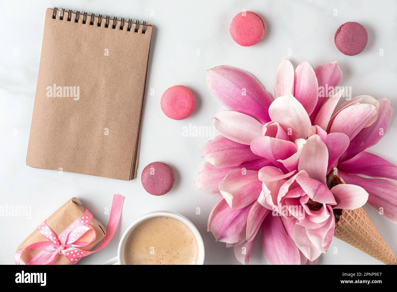 Leeres Notizbuch aus Papier mit Magnolienblüten in Eiskrem, Geschenkbox, Kaffeetasse und Makronen. Hochzeitshintergrund. Modell. Flach verlegt Stockfoto