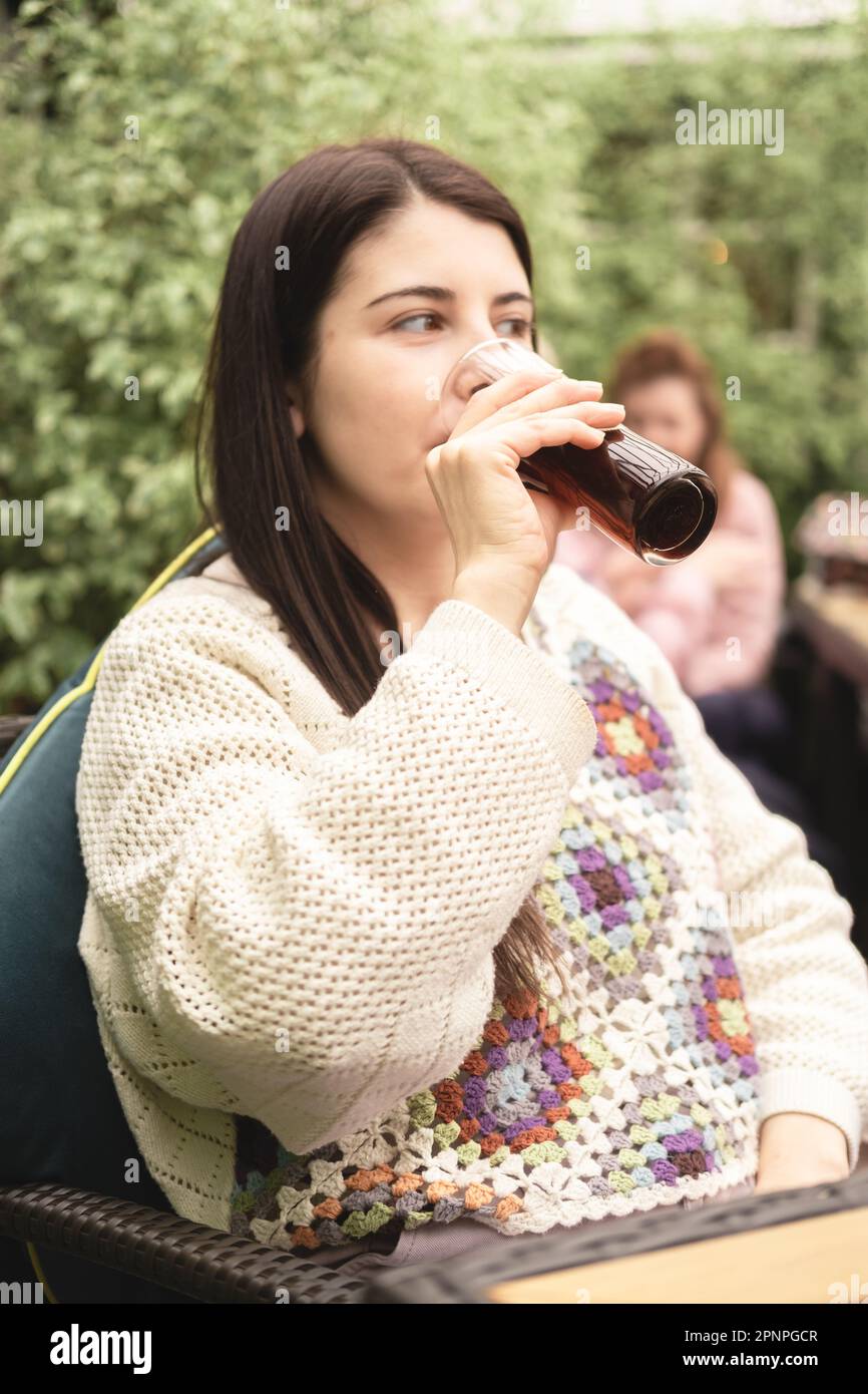 Vertikales Porträt einer wunderschönen brünetten Frau und einer neuen mutter, die nach einem Spaziergang in einem Biergarten im Pub ein alkoholfreies Getränk trinken Stockfoto