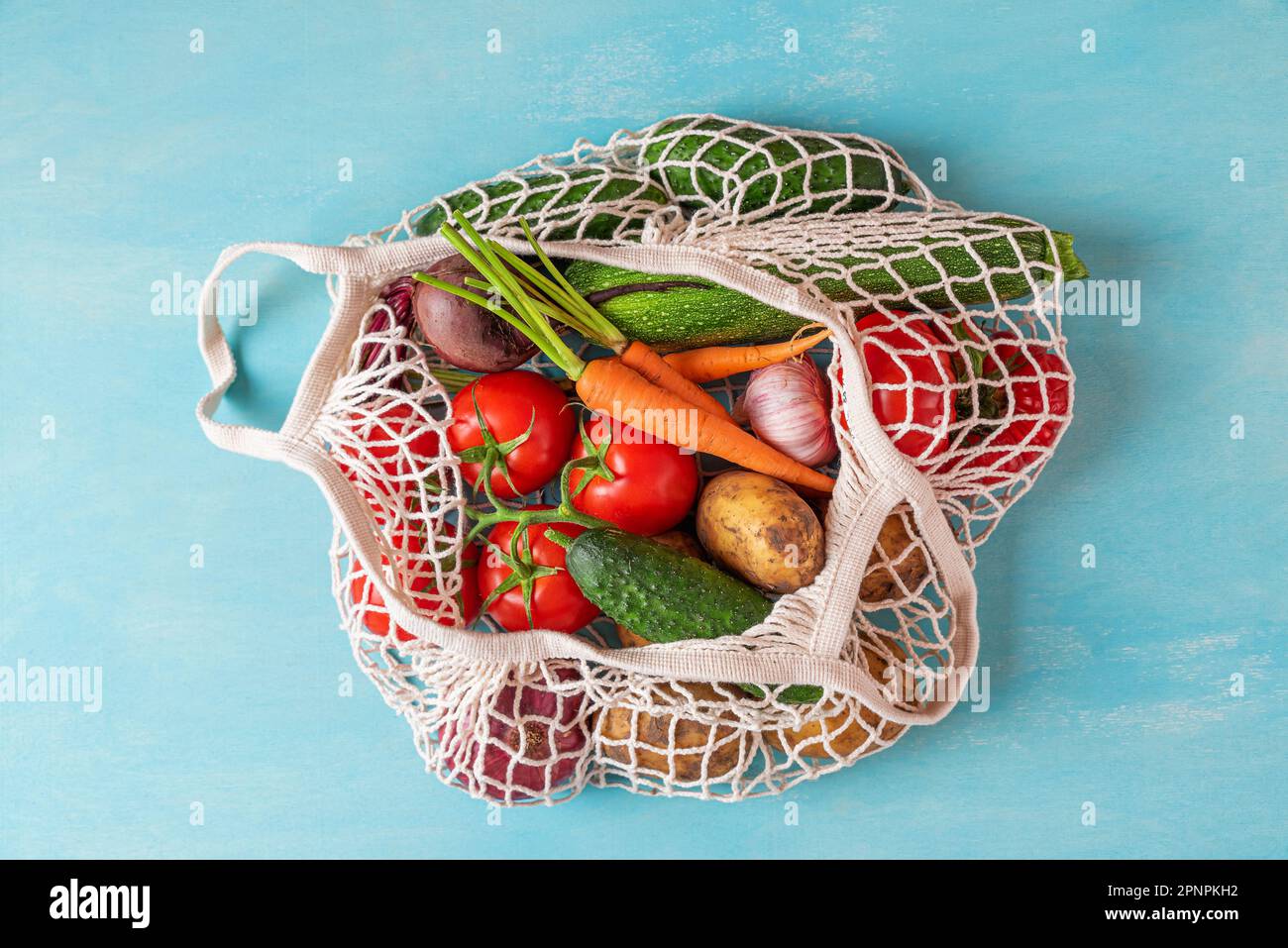 Einkaufstasche aus Mesh mit Bio-Gemüse auf blauem Hintergrund. Nachhaltiger Lebensstil, keine Abfälle, plastikfreies Konzept. Umweltfreundliches Einkaufen Stockfoto