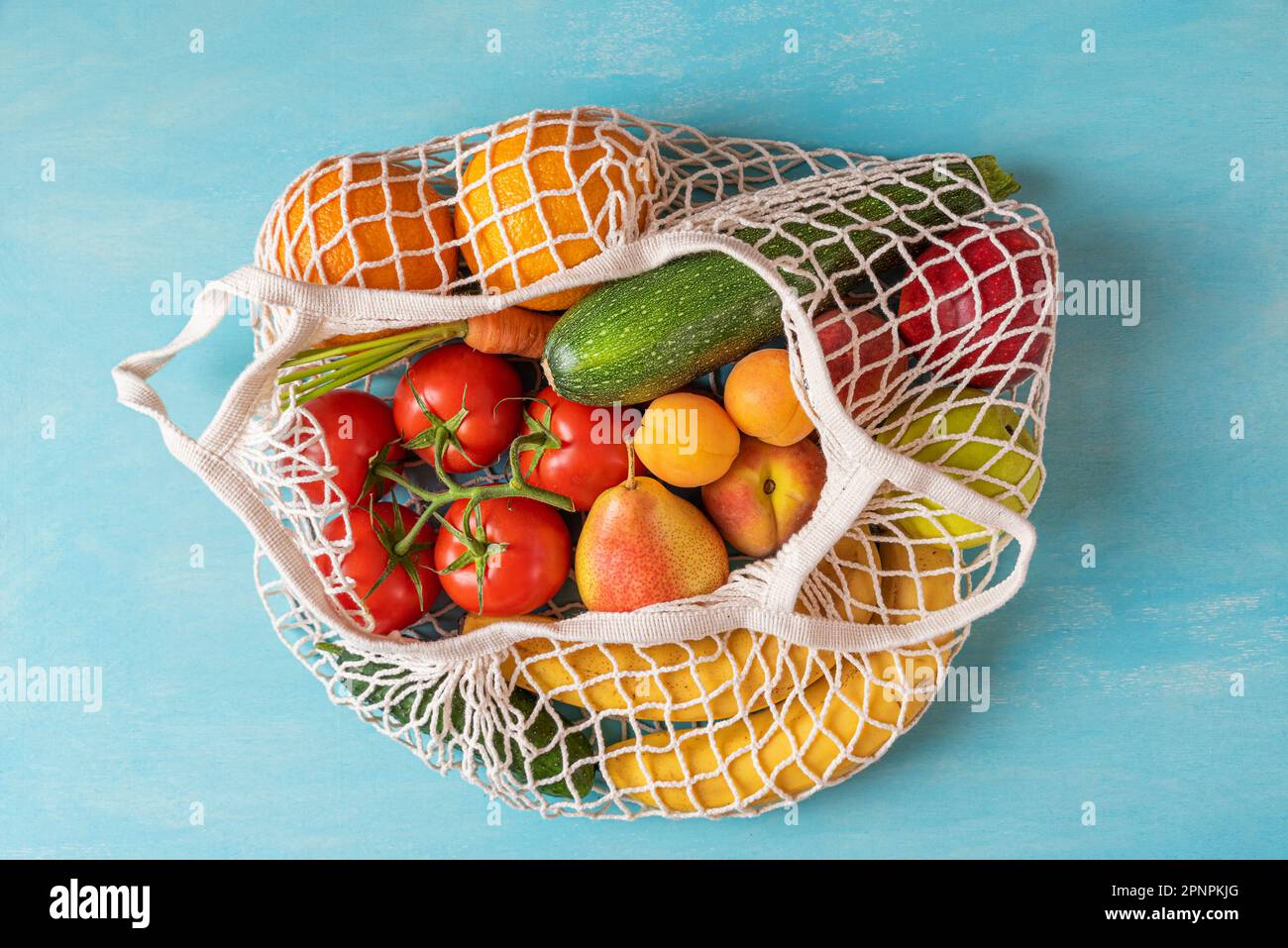 Mesh-Einkaufstasche mit gesunden Bio-Früchten in Gemüse vom Markt auf blauem Hintergrund. Draufsicht. Vegane oder vegetarische Produkte. Nachhaltige li Stockfoto