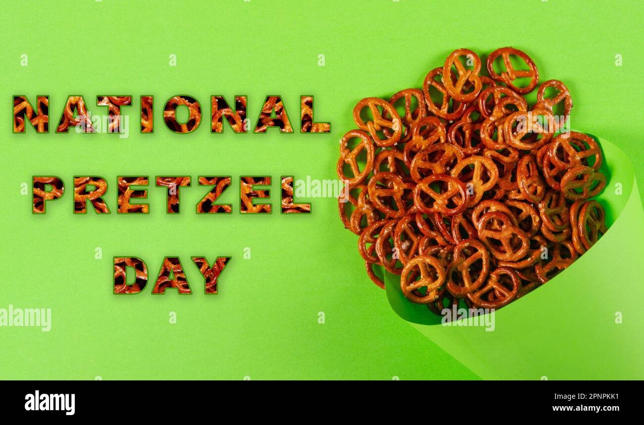 Mini-Brezeln in hellgrünem Papierkegel liegen auf hellgrünem Hintergrund mit dem Text: National Bretzel Day Stockfoto