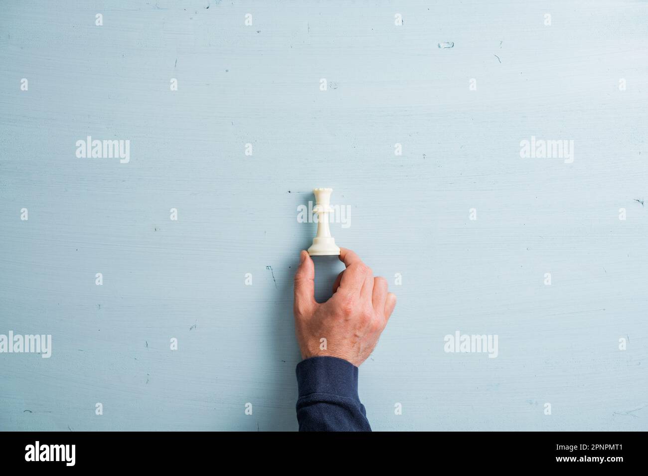 Männliche Hand legt weiße Schachfigur auf einen einfachen hellblauen Holzhintergrund. Mit viel Platz zum Kopieren. Stockfoto