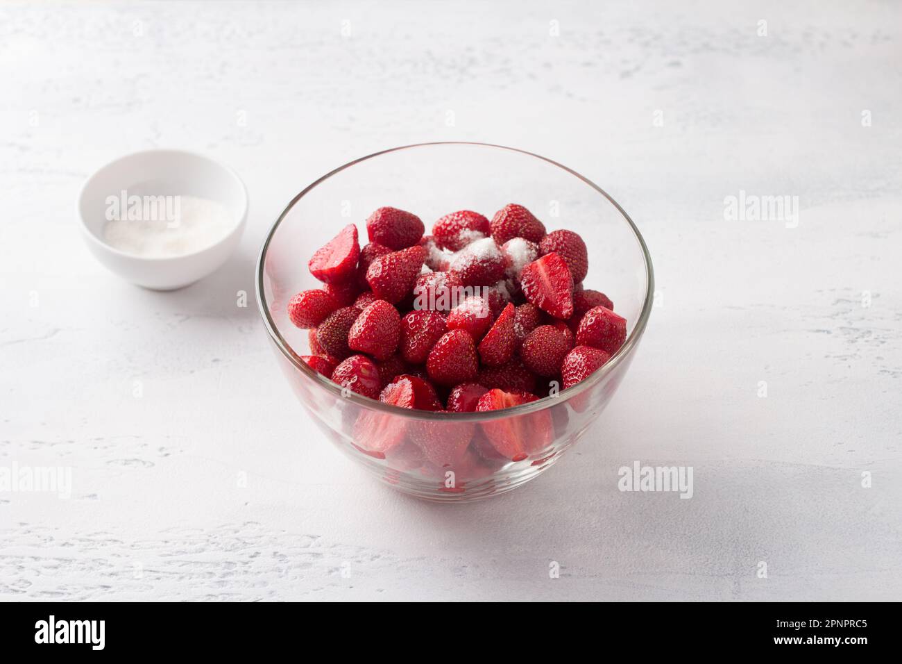 Glasschüssel mit gehackten Erdbeeren und Zucker auf hellblauem Hintergrund Stockfoto