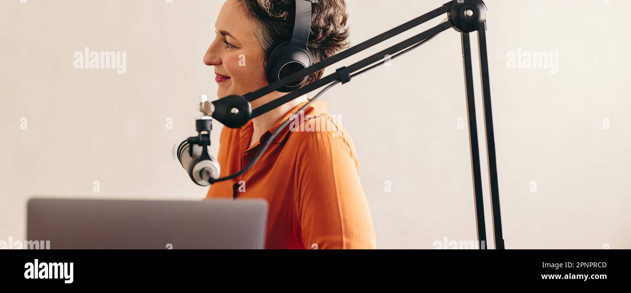 Frau, die einem Gast während eines Interviews in ihrem Podcast zuhört. Weibliche Radiomoderatorin, die eine Live-Audioübertragung in einem Studio moderiert. Eine sitzende Frau Stockfoto