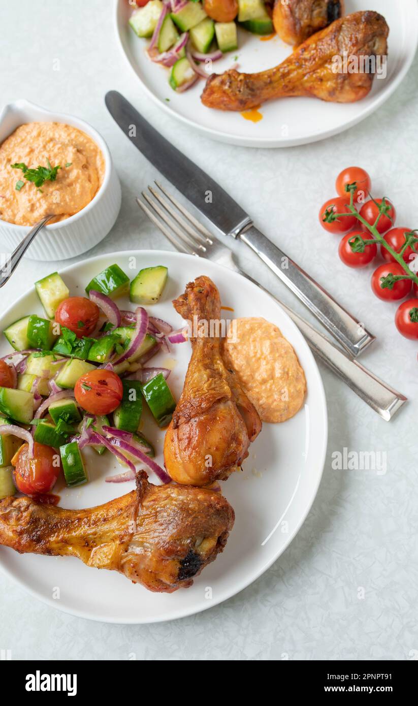 Sommer-Abendessen oder Mittagessen mit gebackenen Hähnchenschenkeln und Fetakäse, Paprika Dip. Serviert mit einer frisch marinierten Zucchini und Tomatensalat Stockfoto