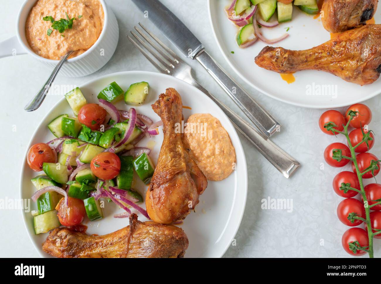 Gebackene Hähnchenschenkel mit Salat und Paprika Feta Dip auf einem Teller Stockfoto