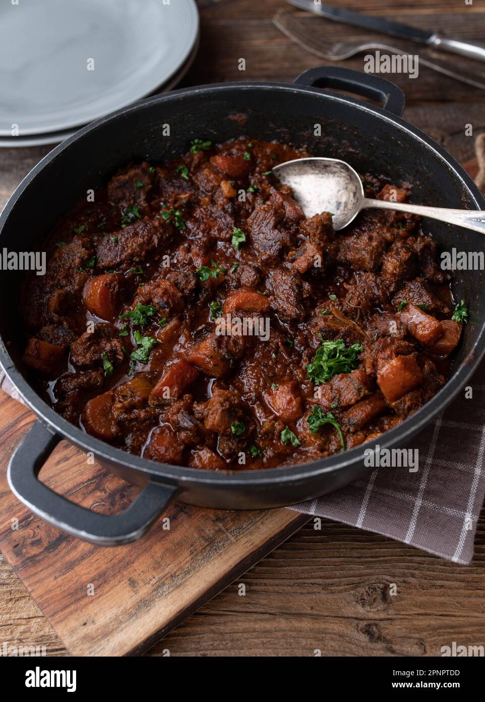 Geschmortes Schweinefleisch mit Karotten und Soße in einem Topf auf einem Holztisch Stockfoto