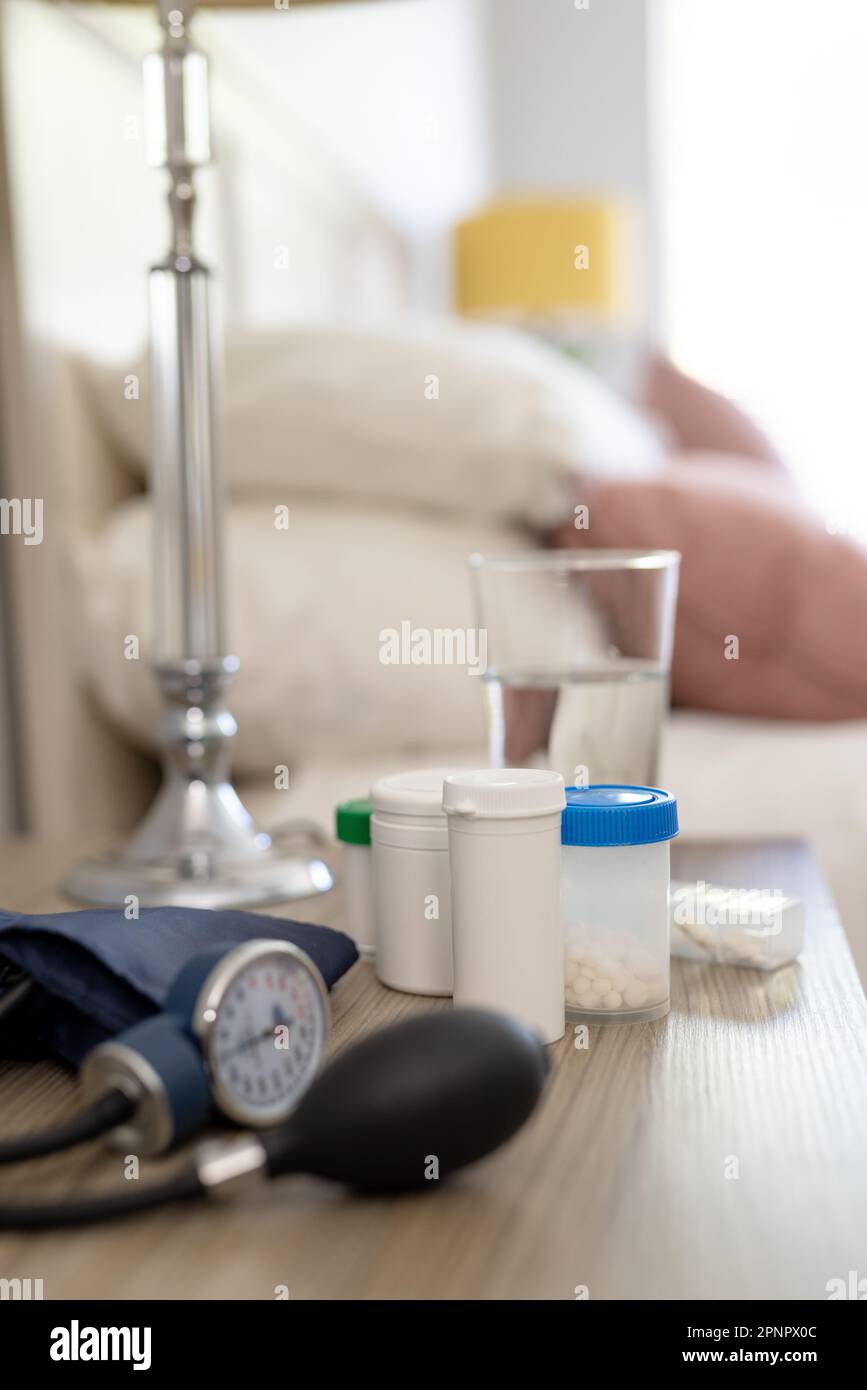 Nahaufnahme von Medikamenten, Blutdruckmessgerät und ein Glas Wasser auf dem Nachttisch im Schlafzimmer Stockfoto