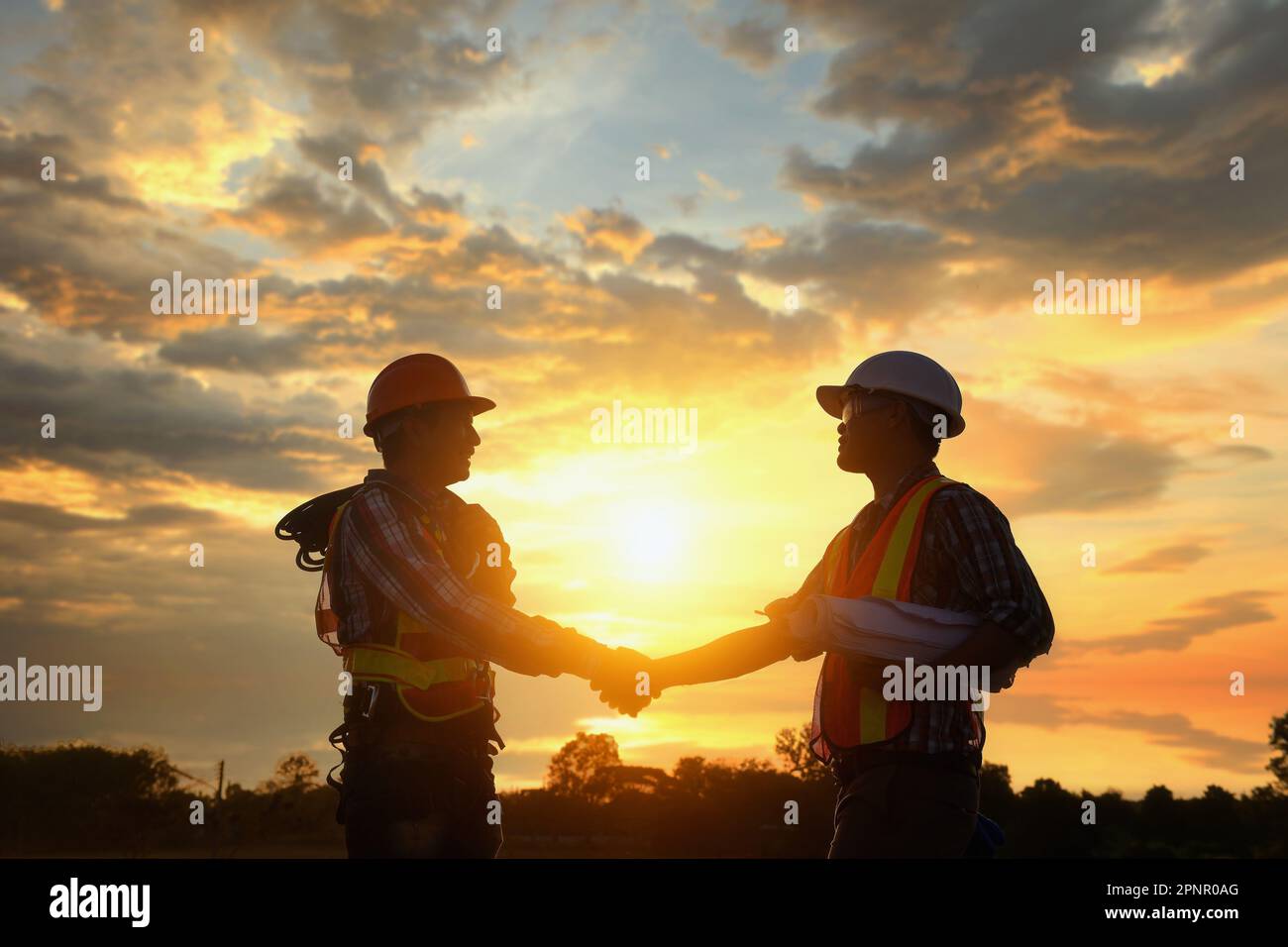 Silhouette von zwei Ingenieuren auf einer Baustelle, die bei Sonnenuntergang in Thailand die Hand schütteln Stockfoto