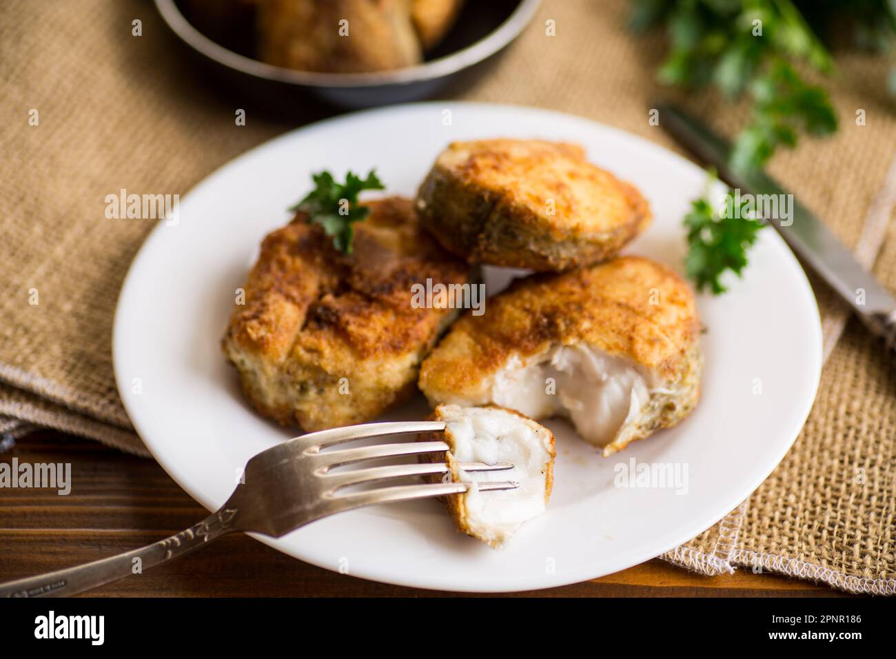 Ein Stück Seehecht, gebraten in knuspriger Kruste, auf einem Teller auf einem Holztisch. Stockfoto