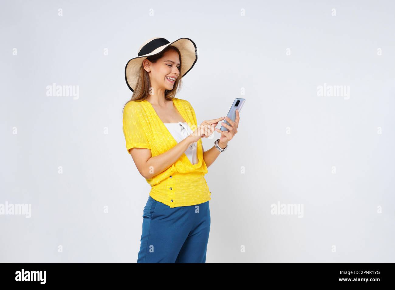 Eine junge Frau, die ein Handy hält und lächelt und einen Sonnenhut und eine Sonnenbrille trägt, isoliert auf weißem Hintergrund. Stockfoto
