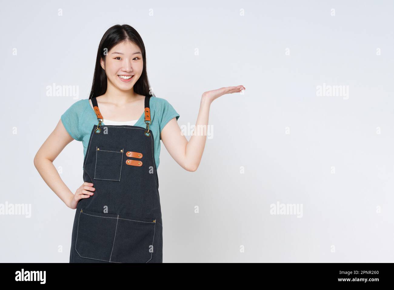 Junge Frau trägt Küchenschürze, präsentiert oder zeigt offene Handfläche mit Kopierbereich für das Produkt isoliert auf weißem Hintergrund. Stockfoto