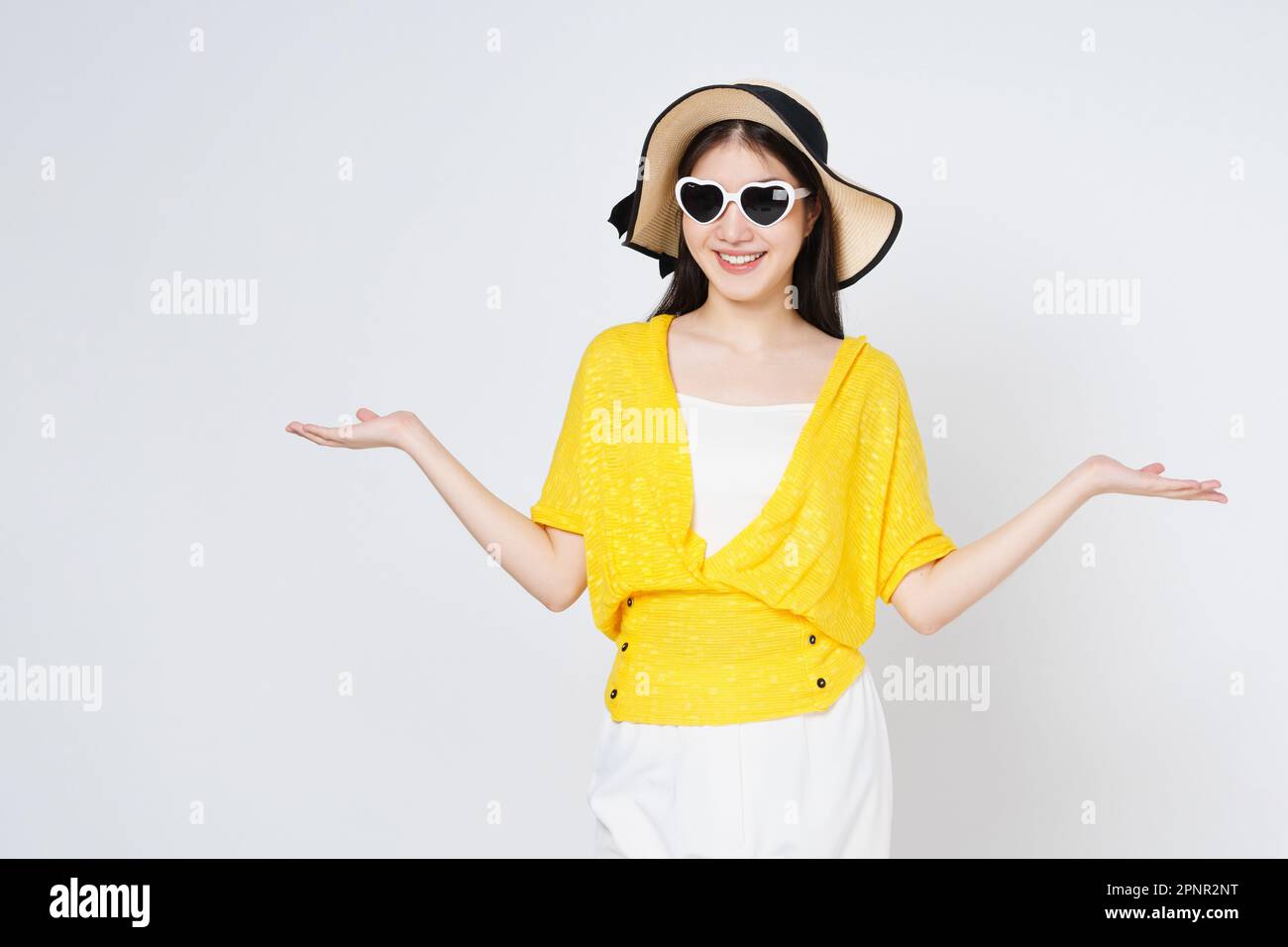 Eine junge Frau mit Sonnenhut und Sonnenbrille, die eine Handfläche mit offenem, isoliertem Kopierbereich für das Produkt auf weißem Hintergrund präsentiert oder zeigt. Stockfoto