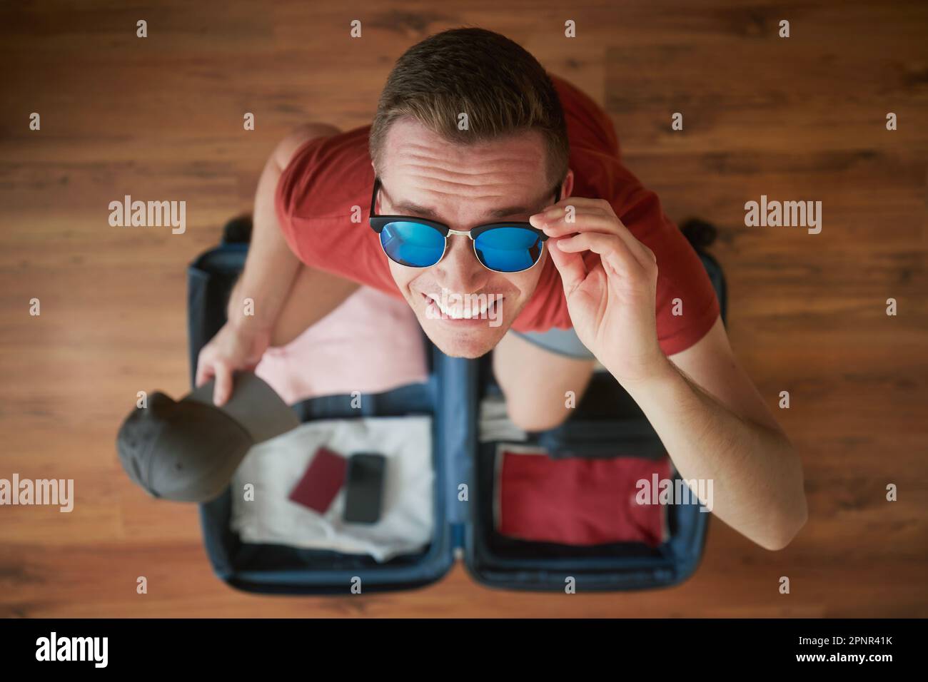 Koffer packen und Sommerabenteuer planen. Porträt eines glücklichen lächelnden Mannes mit Sonnenbrille, der über offenem Gepäck in die Kamera schaut. Stockfoto