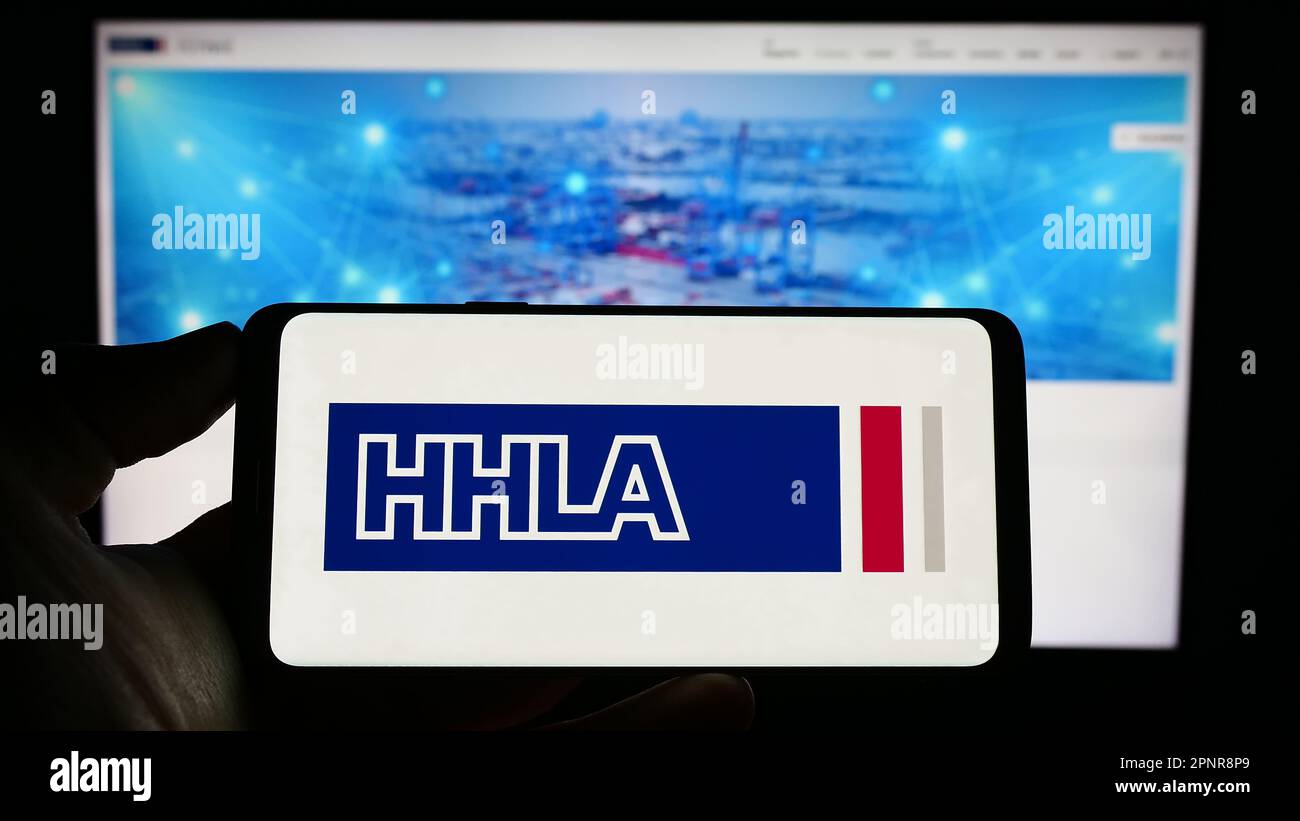 Person, die ein Mobiltelefon mit dem Logo der Firma Hamburger Hafen und Logistik AG (HHLA) auf dem Bildschirm vor der Webseite hält. Konzentrieren Sie sich auf das Display des Telefons. Stockfoto