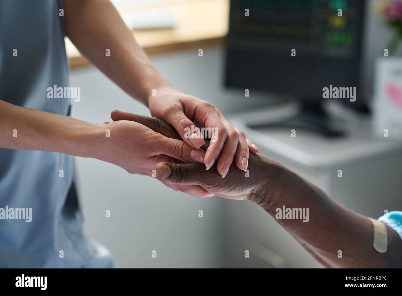 Nahaufnahme einer jungen Ärztin, die Händchen mit einem afroamerikanischen Patienten hält, während er auf der Station liegt Stockfoto