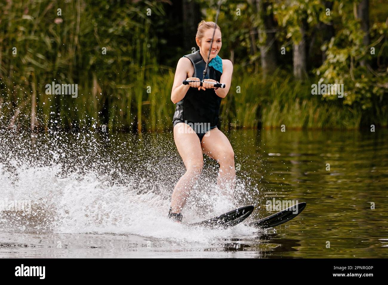 Wunderschöne junge Frau, die hinter einem Motorboot auf dem See Wasserski fährt, extreme Wassersportarten, Sommerurlaub Stockfoto