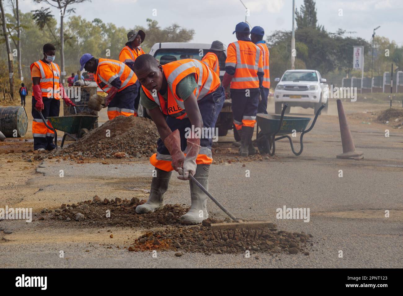 Trymore Sagwati und seine Kollegen füllen Schlaglöcher mit Sand und Zement in Ruwa, Simbabwe. Die Regierung hat begonnen, Straßen zu reparieren, um Unfälle und Schäden an Fahrzeugen zu reduzieren. (Vimbai Chinembiri/Global Press Journal) Stockfoto