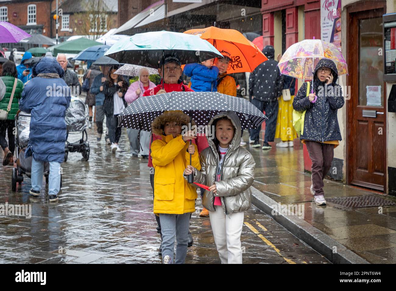 Orientalischer Familienspaziergang entlang einer Dorfstraße unter Sonnenschirmen im Regen Stockfoto